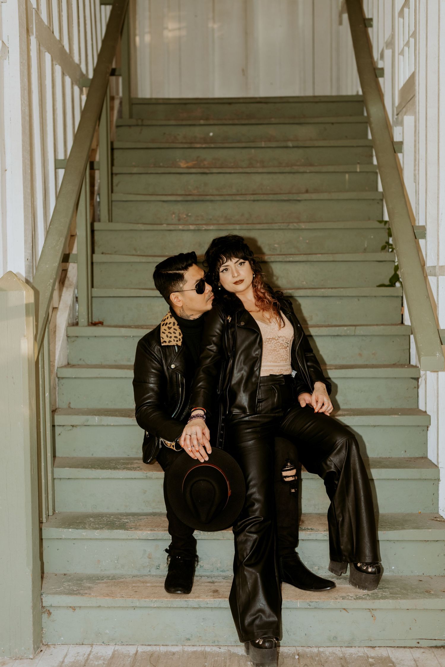 Couple in matching black leather jackets sitting intimately on vintage green stairs.
