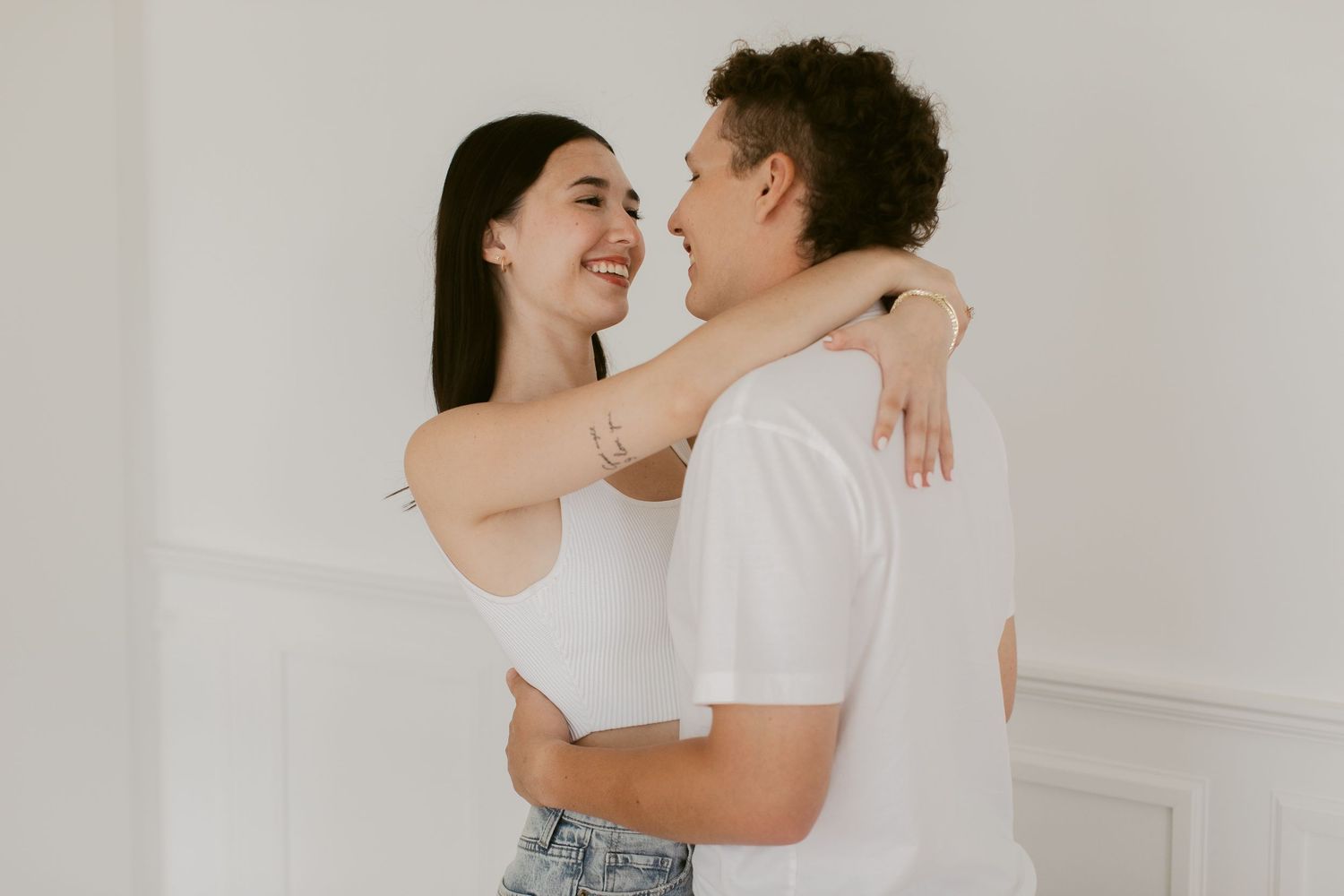 Happy couple in white tops sharing a warm embrace and smile in a bright white room.