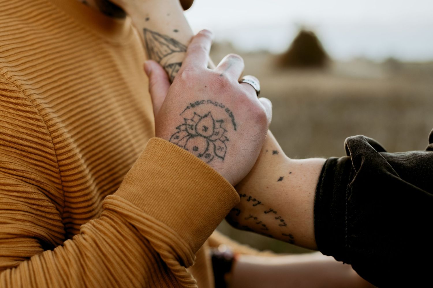 Couple holding hands, displaying beautiful floral and script tattoos on their hands and wrists.