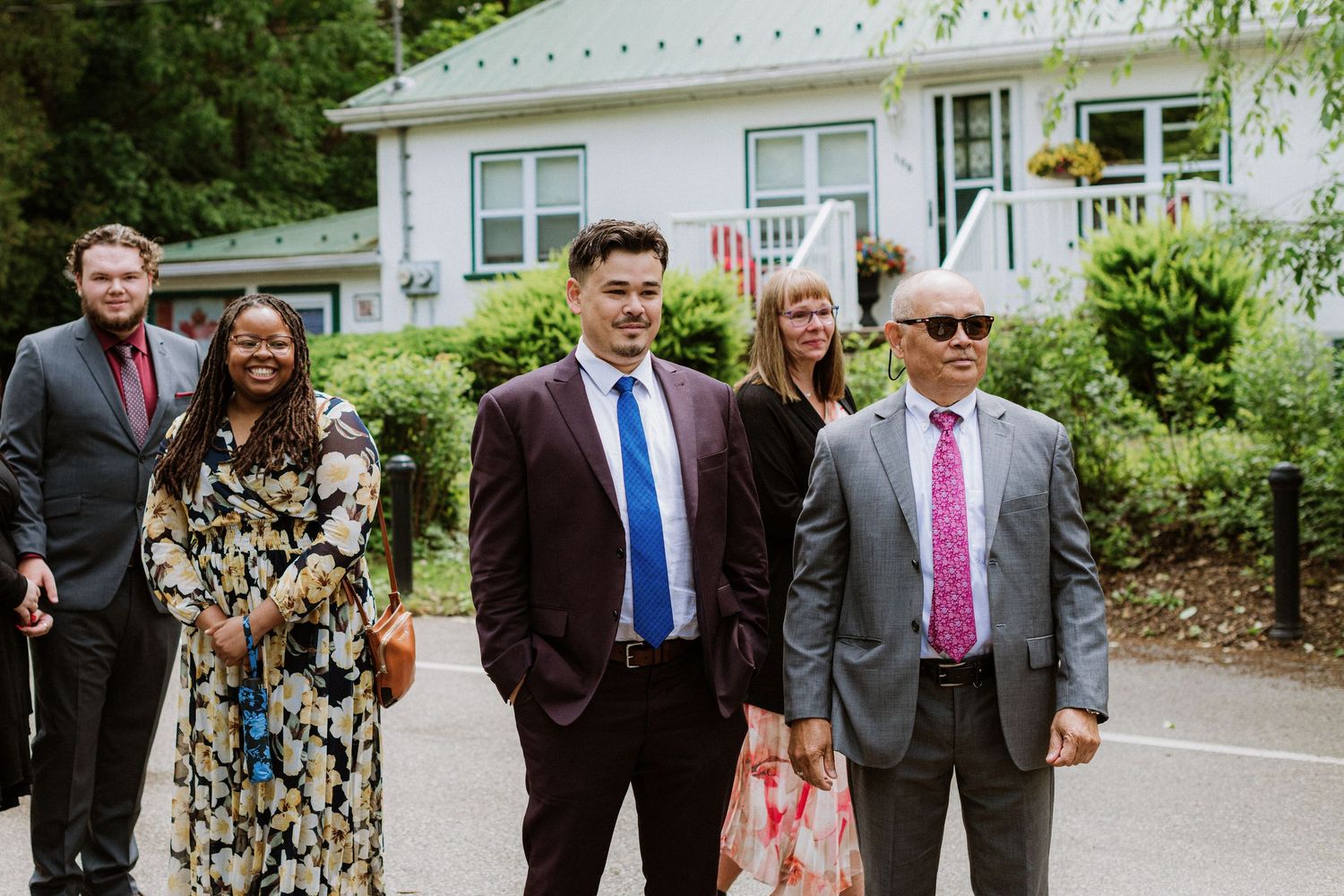 Smiling wedding guests dressed in formal attire walk together along a path at an outdoor venue.