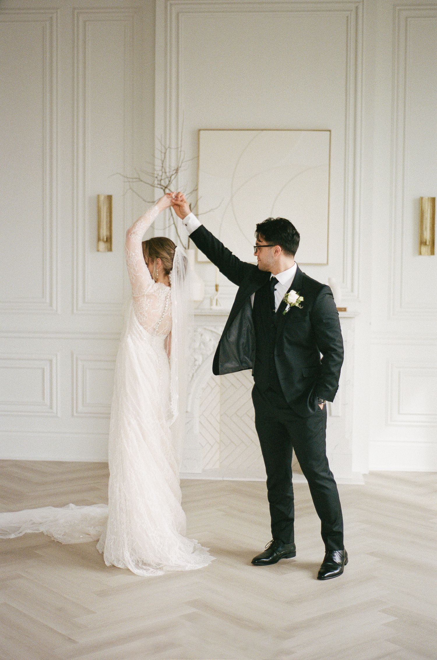Bride and groom share a romantic first dance in an elegant white ballroom with gold sconces.