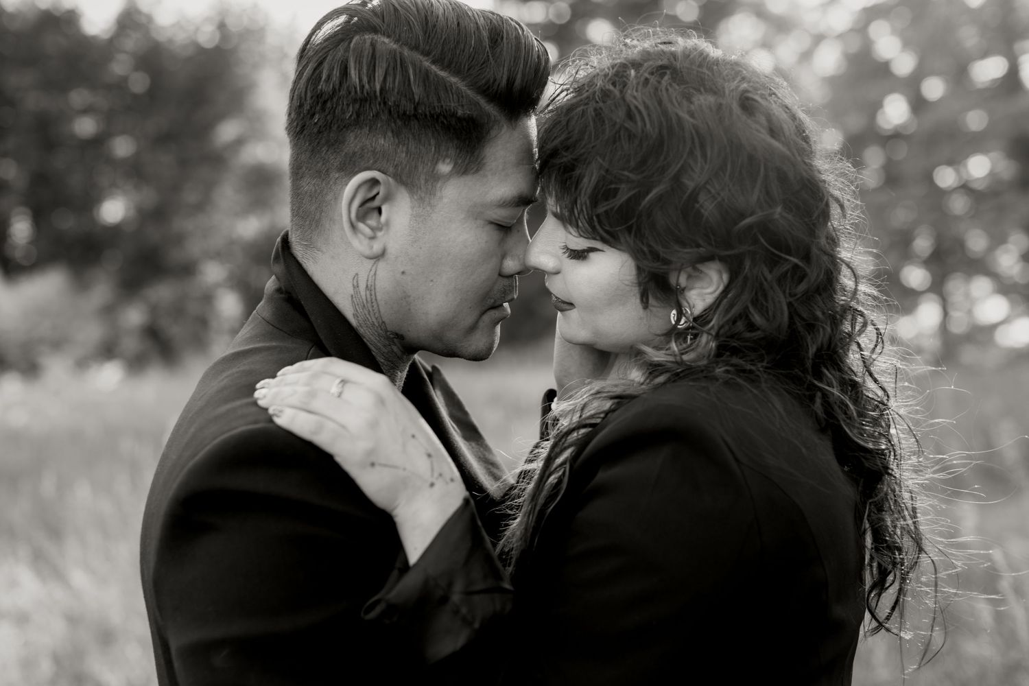 Black and white photo of a romantic couple embracing closely in a field.