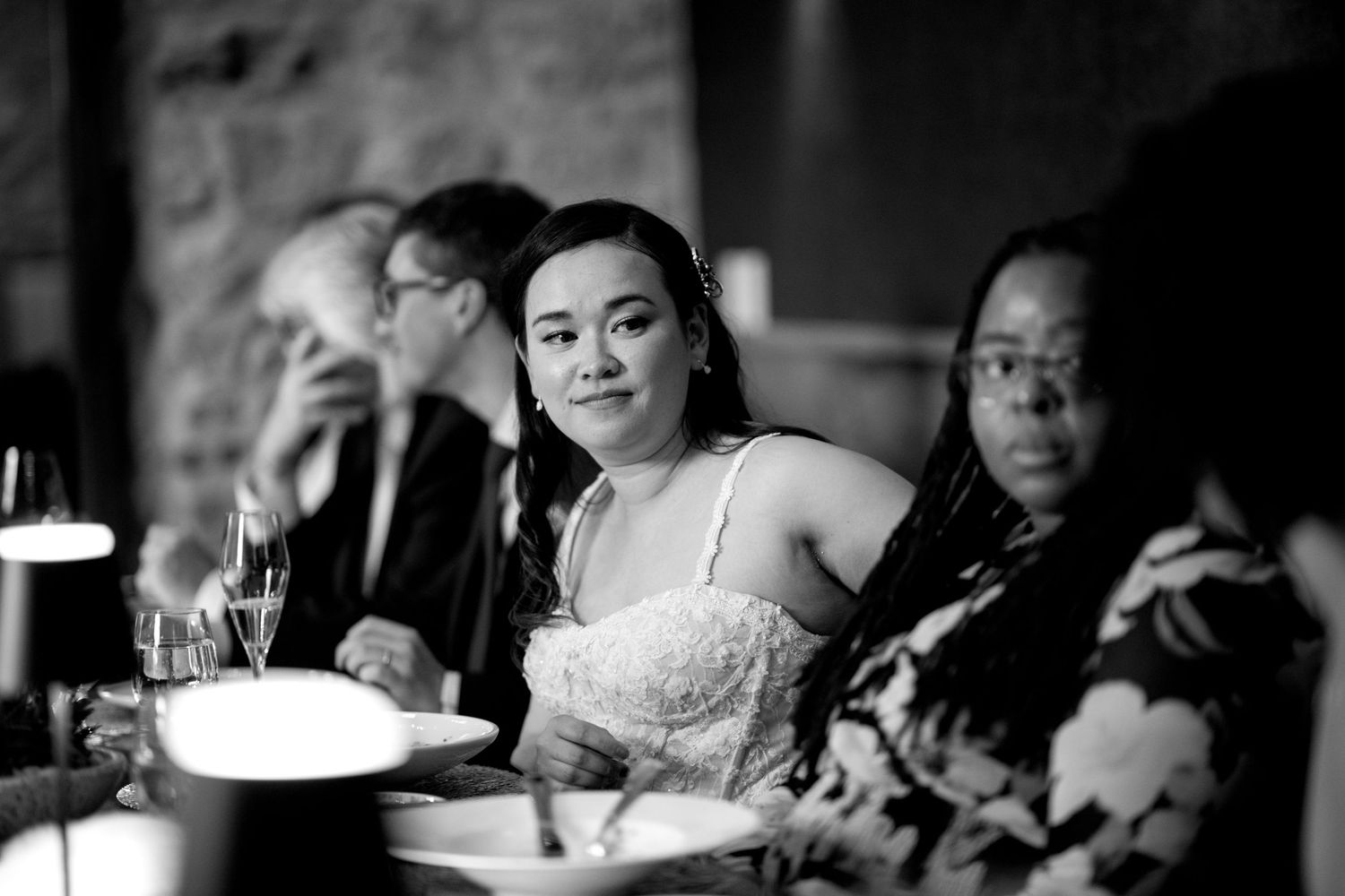 Bride in white lace dress seated at elegant wedding reception dinner table in black and white photo.