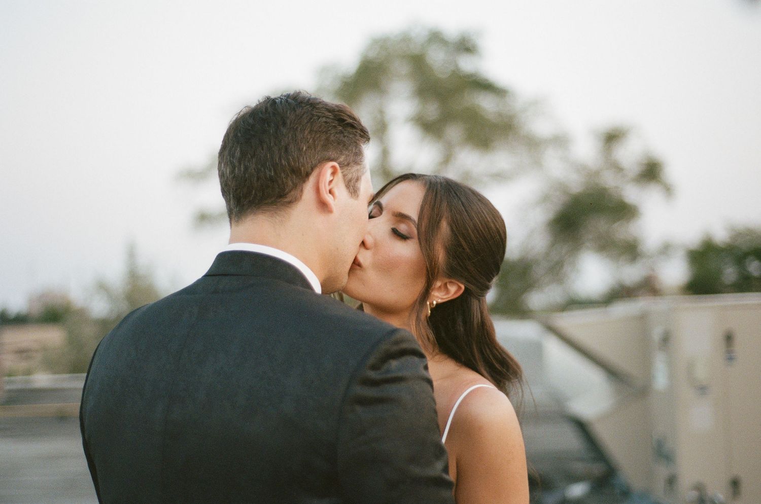 Bride and groom sharing a romantic kiss outdoors at dusk during their wedding celebration.