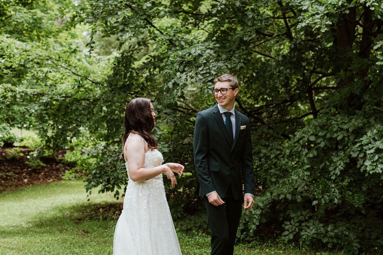 Bride and groom sharing emotional first look moment surrounded by green trees.