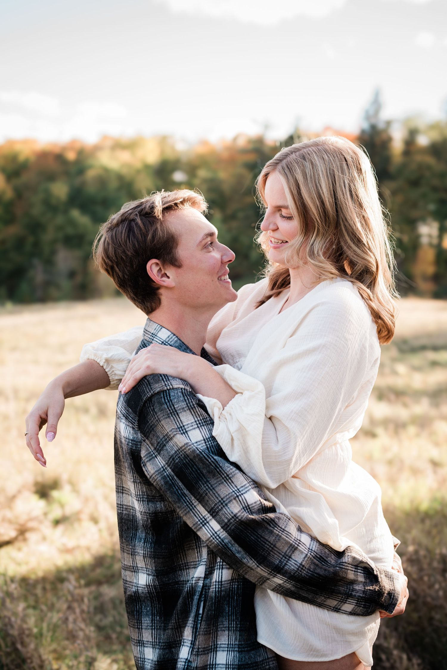 Happy couple laughing and embracing in golden sunlit field during autumn season.