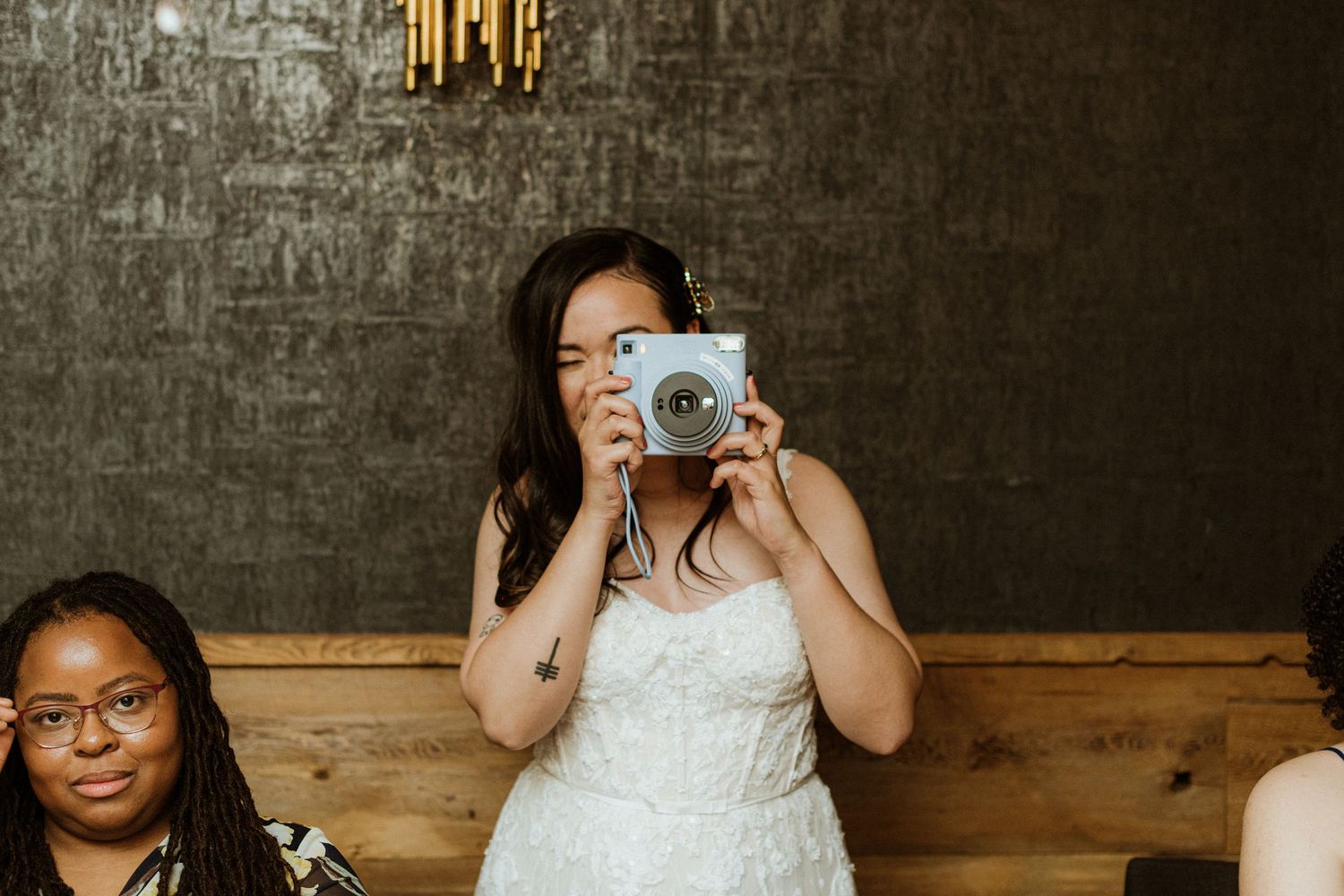 Bride in white gown takes photo with instant camera at wedding reception dinner.