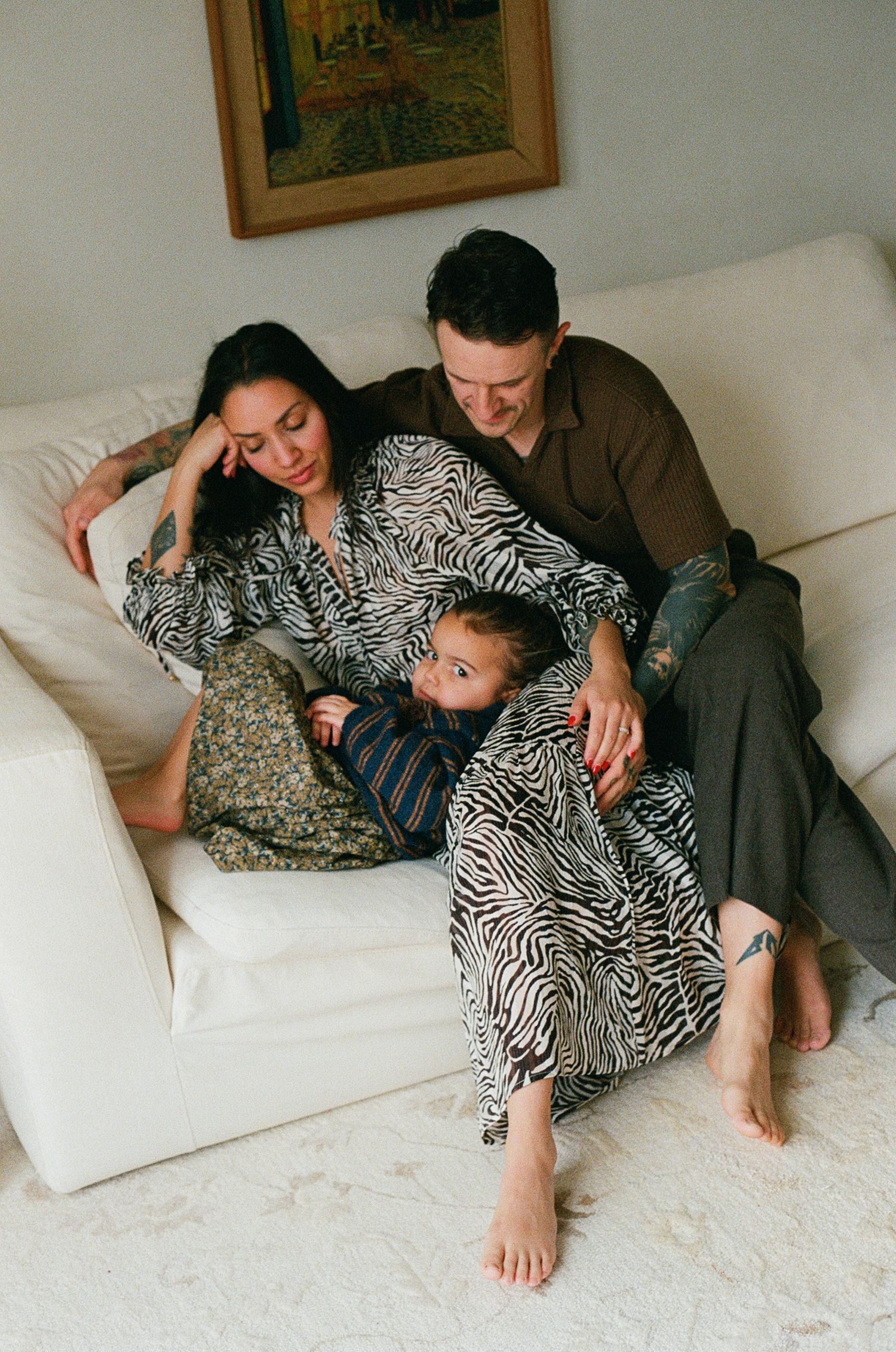Family of three relaxing together on white couch with child between parents at home.
