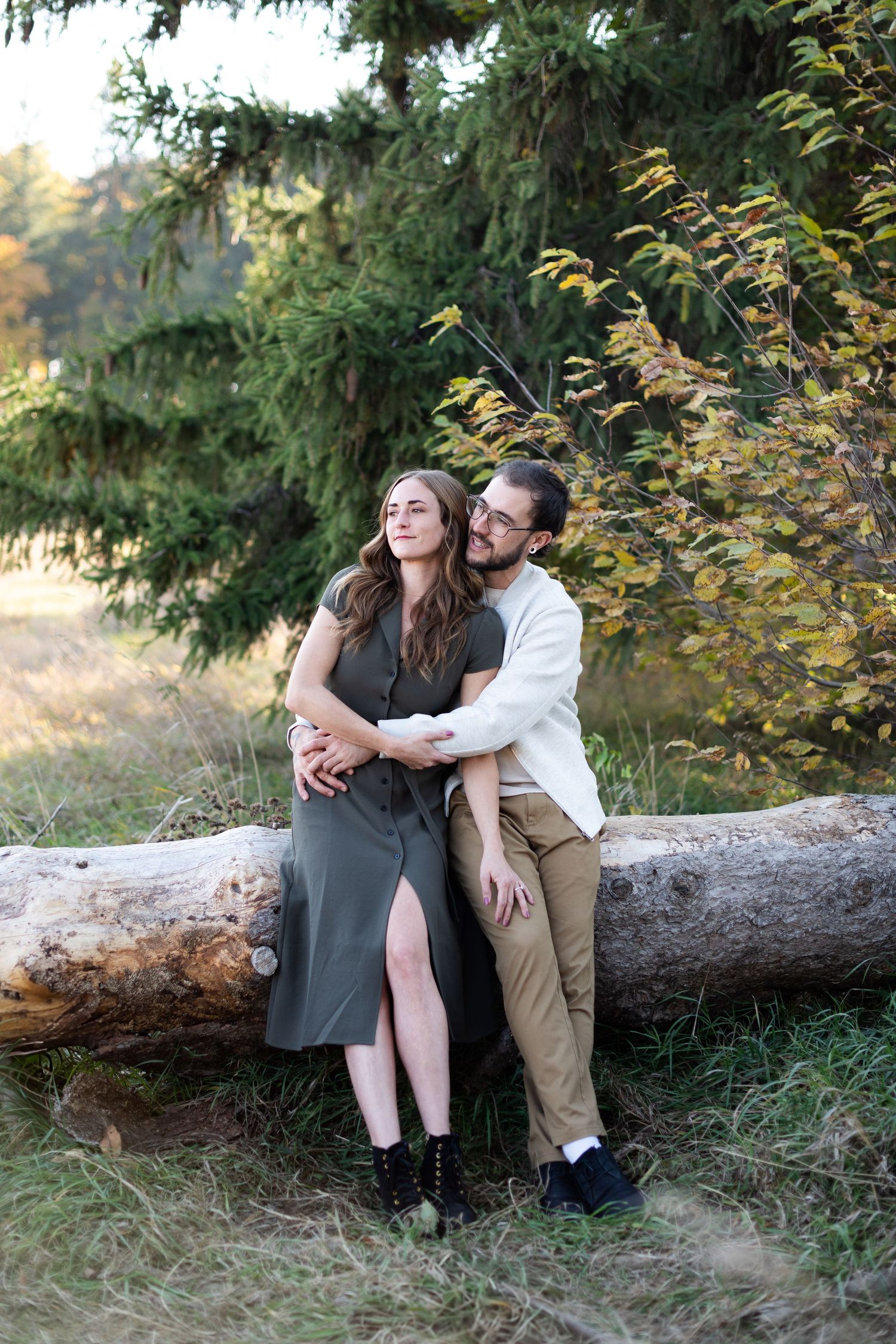 Couple leaning against a fallen log in a forest, embracing during an outdoor engagement session.