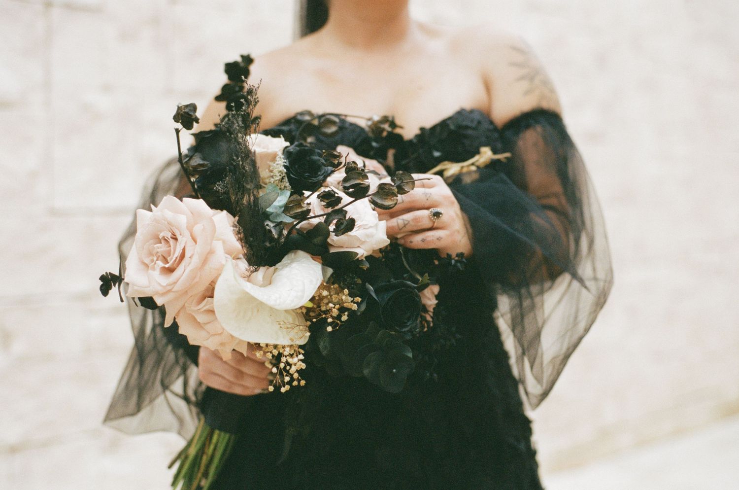 Close-up of bride holding dark and blush floral bouquet in black lace off-shoulder gown.