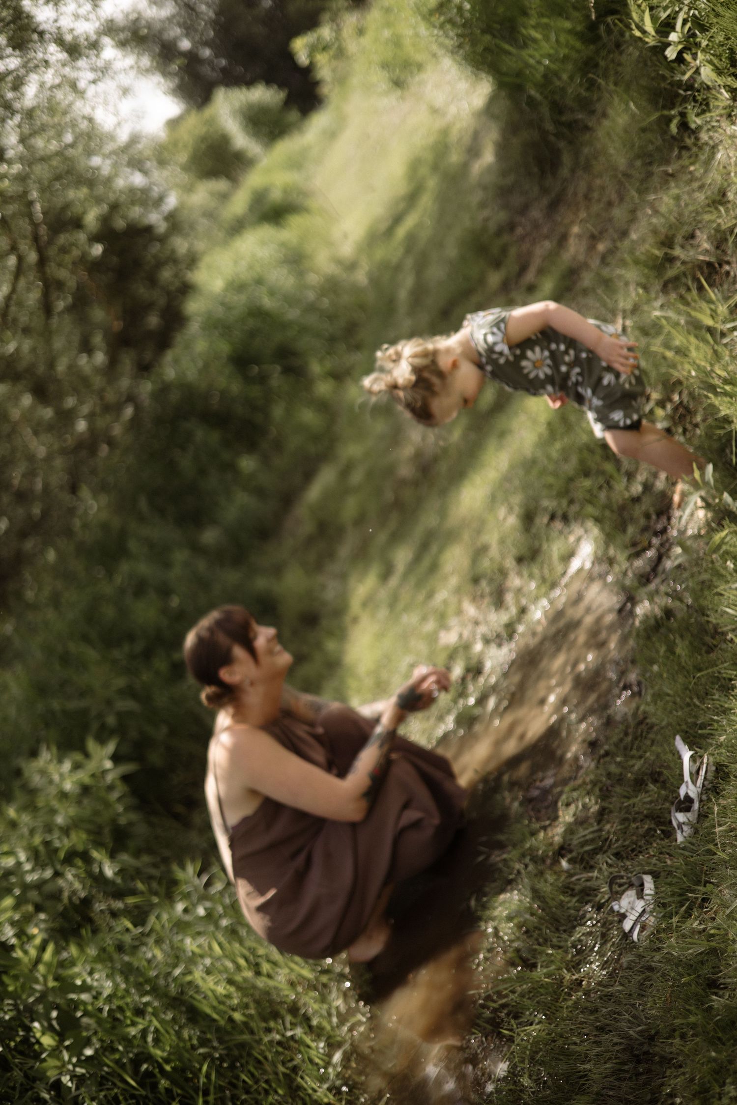 Blurred action shot of mother catching leaping toddler girl in daisy outfit on green hillside.