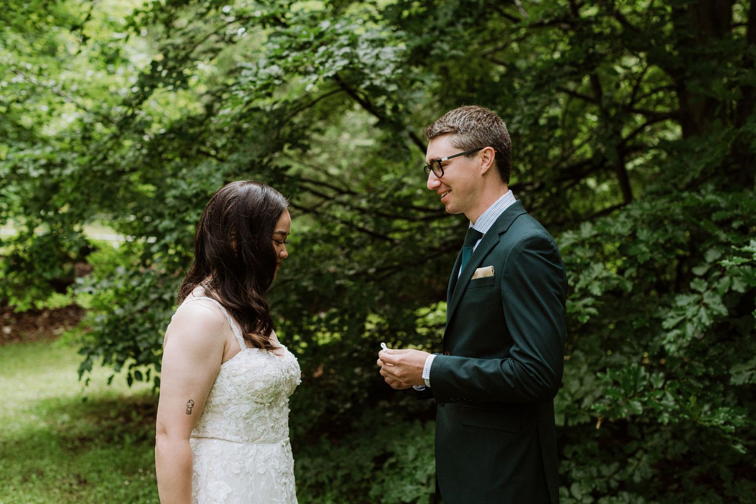 Bride and groom facing each other during heartfelt first look in wooded setting.