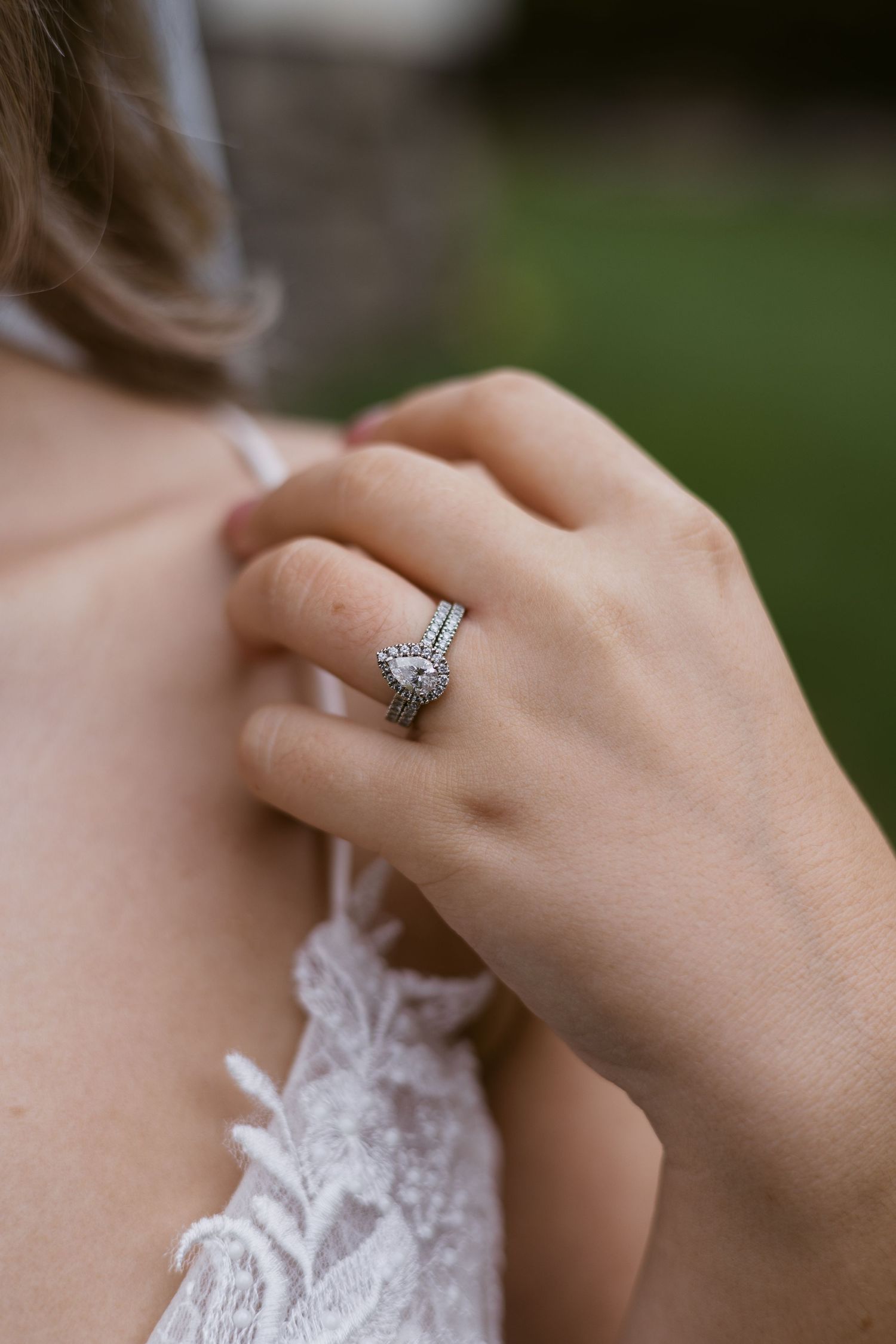Close-up of bride's hand showing pear-shaped diamond halo engagement ring with wedding band.
