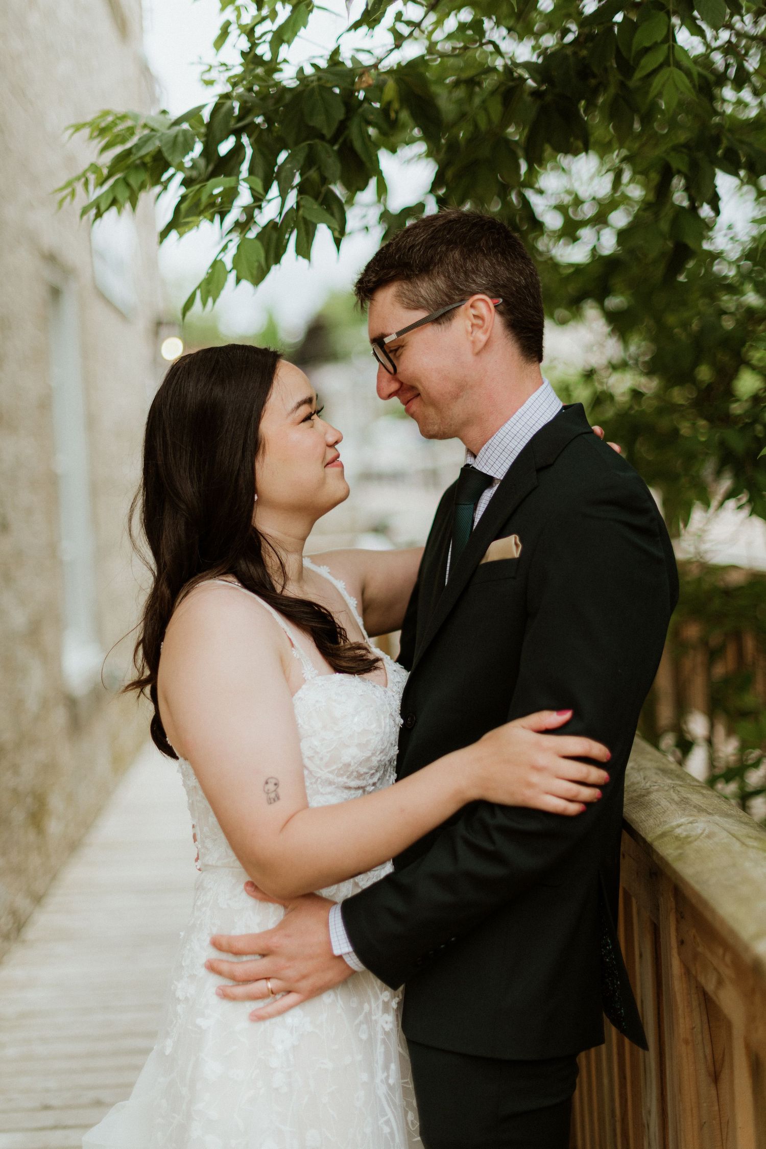 Bride and groom gazing into each other's eyes while embracing near a wooden railing outdoors.