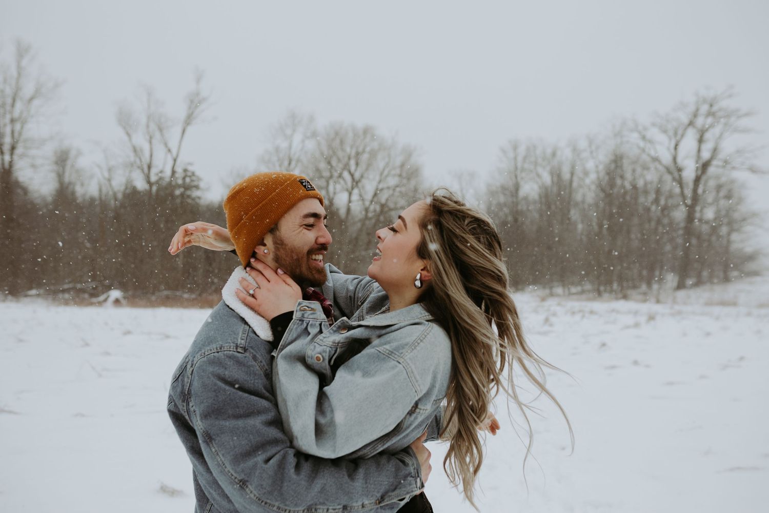 Joyful couple embracing and laughing together in snowy field during winter snowfall.