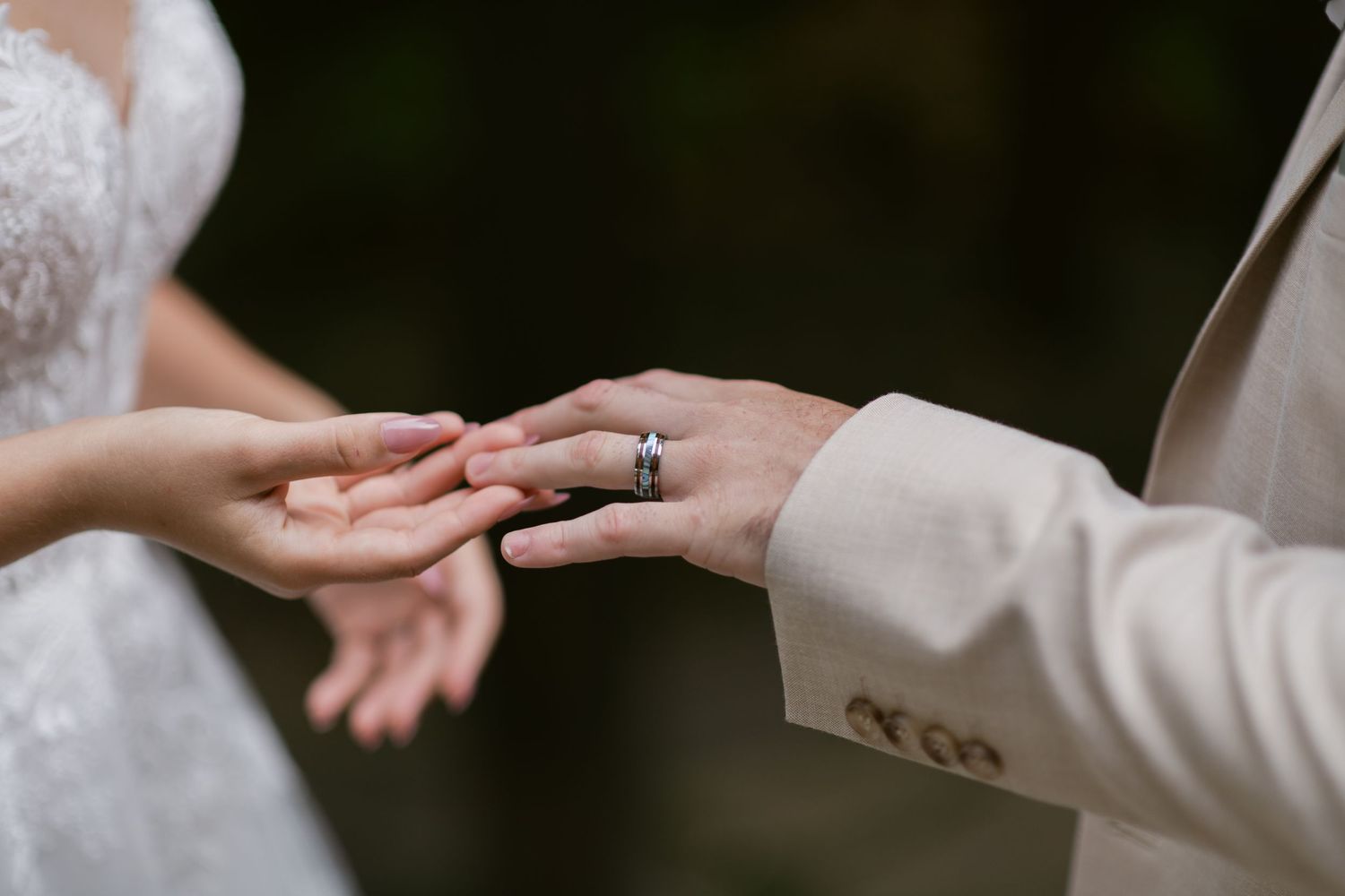 Close-up of groom placing a wedding ring on bride's finger during an outdoor ceremony.