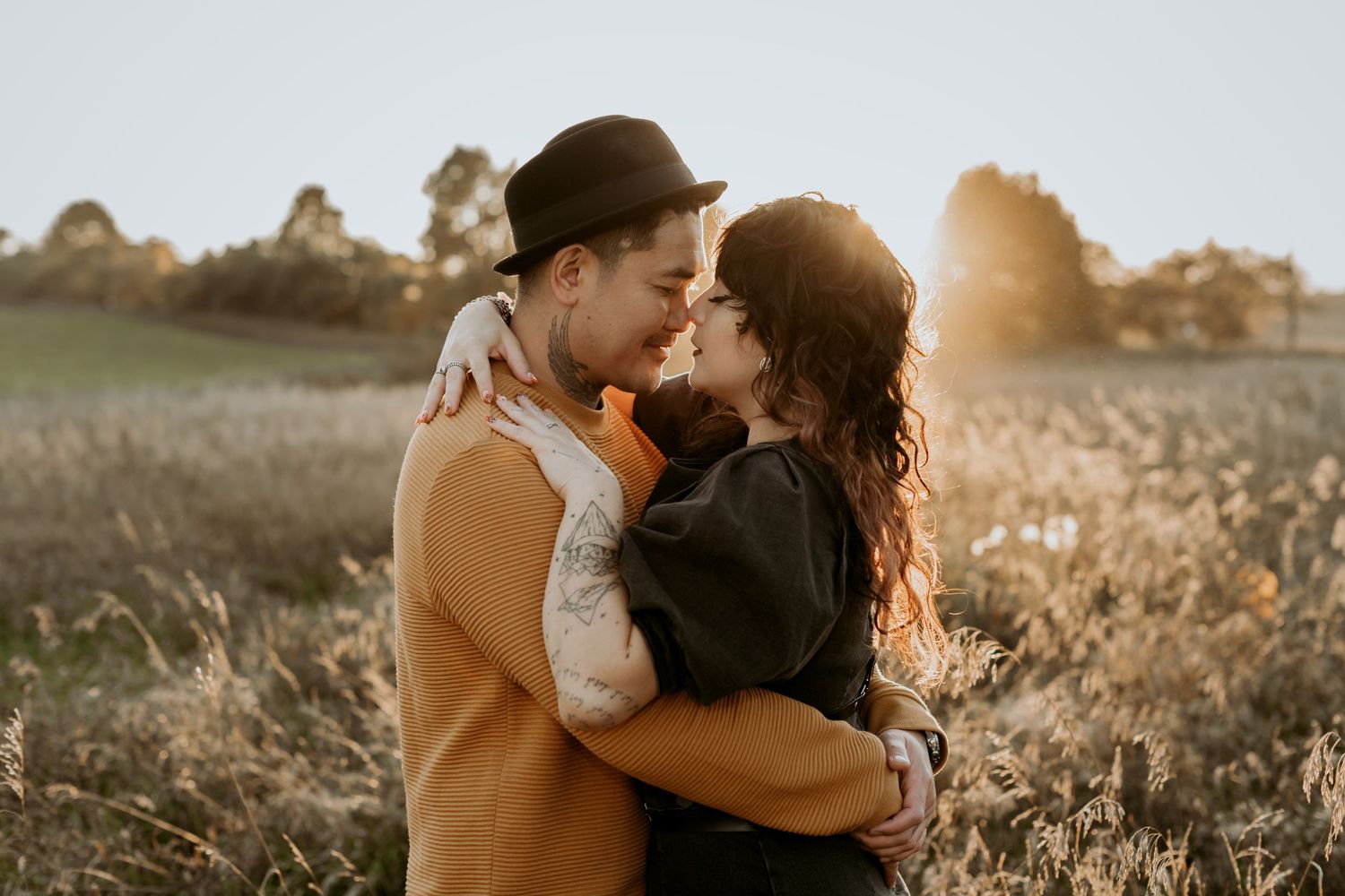Couple sharing a kiss in an open field bathed in warm golden sunset light.