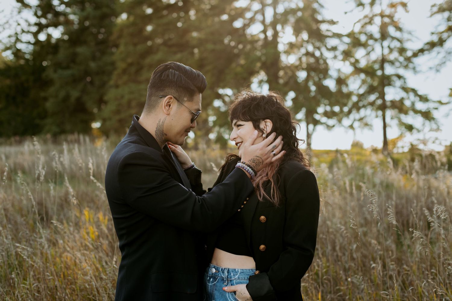 A couple laughing together in a golden meadow, man tenderly holding womans face in his hands.