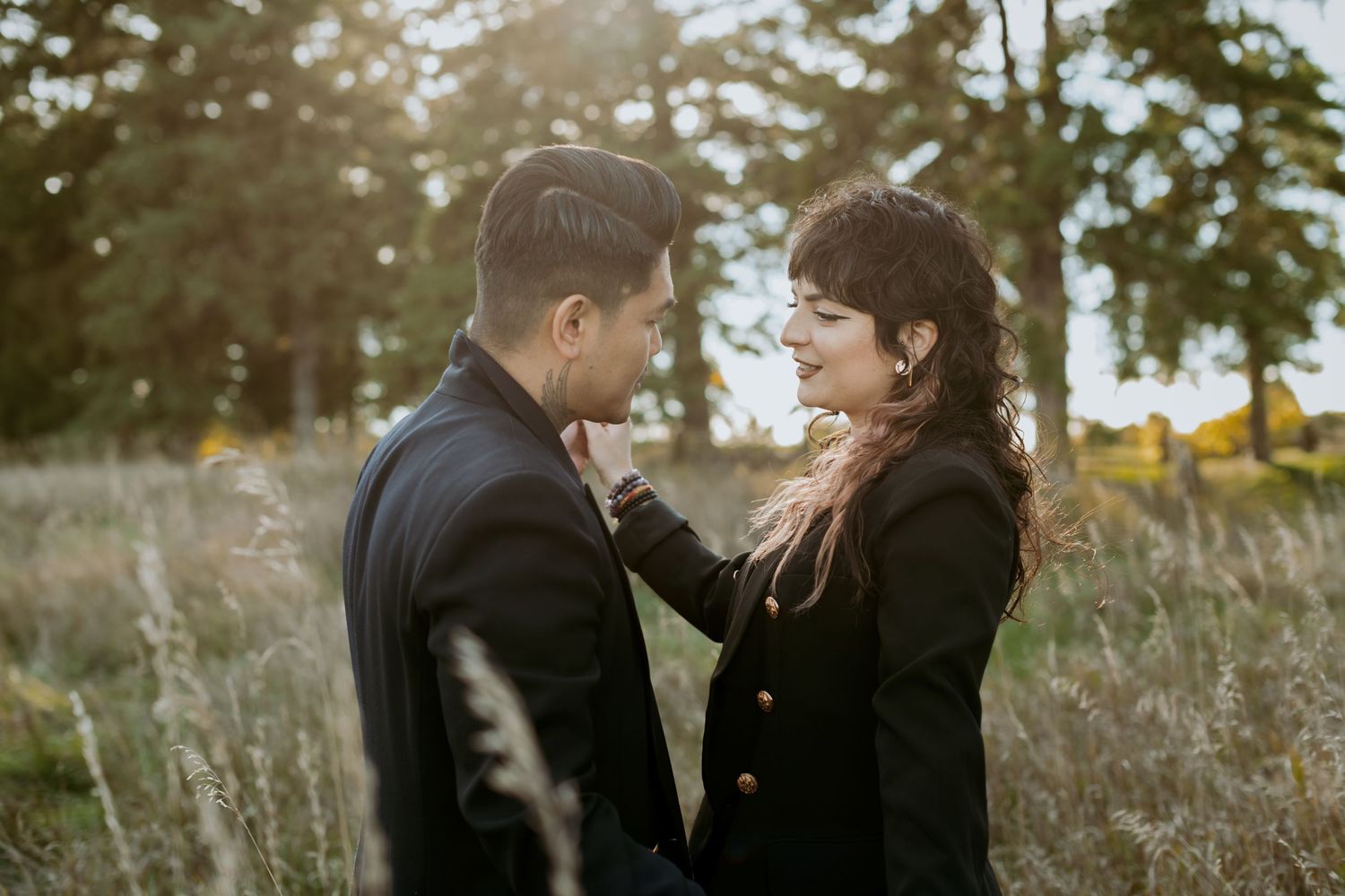 Couple in black outfits share a tender moment in a golden field at sunset.