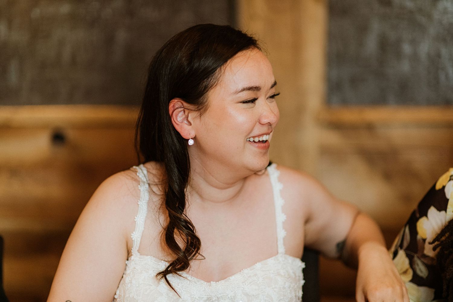Bride in white lace dress laughing joyfully at wedding reception dinner.