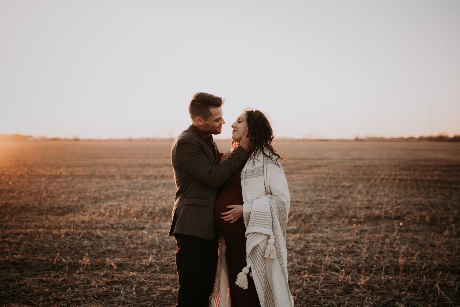 Couple shares romantic moment together in open field during golden hour maternity session.