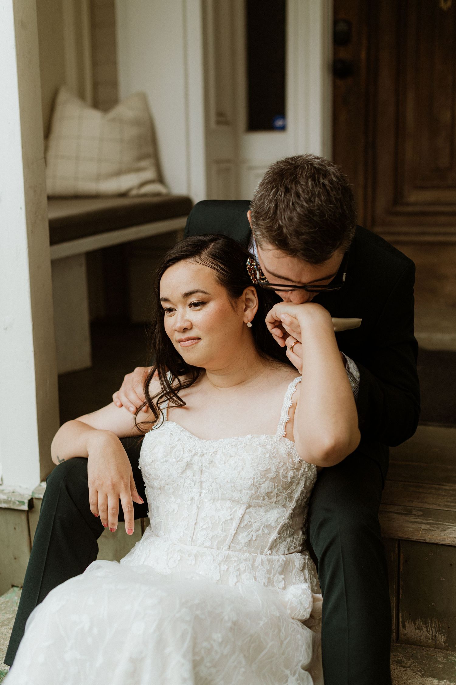 Groom leans in to whisper to bride as they sit together on vintage porch steps.