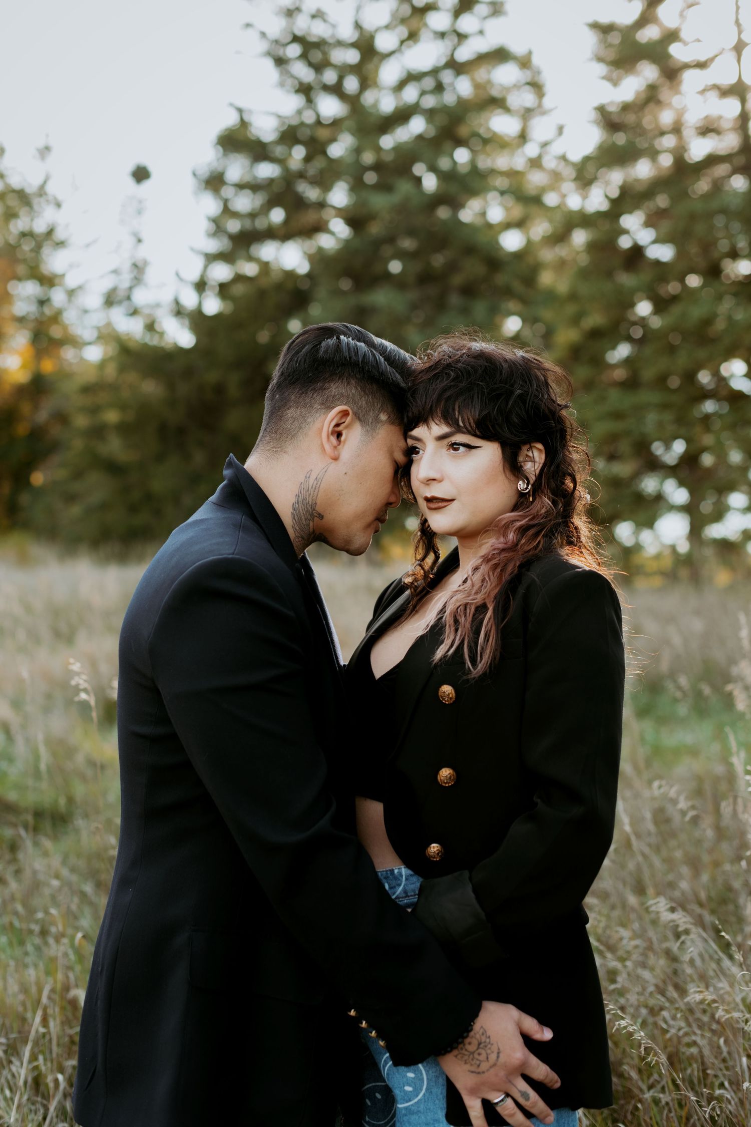 A couple in black outfits sharing an intimate forehead touch in a golden grass field.