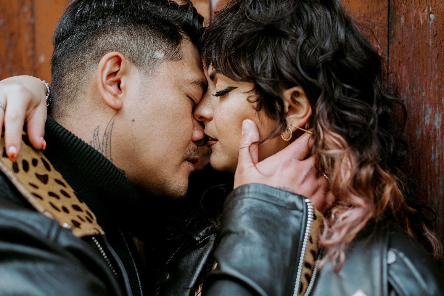 Close-up of couple sharing a kiss against a rich brown wooden door.