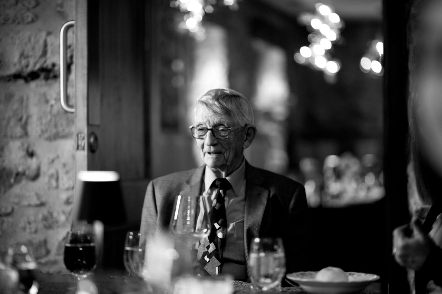 Elderly man in suit seated at wedding reception dinner table in black and white photo.