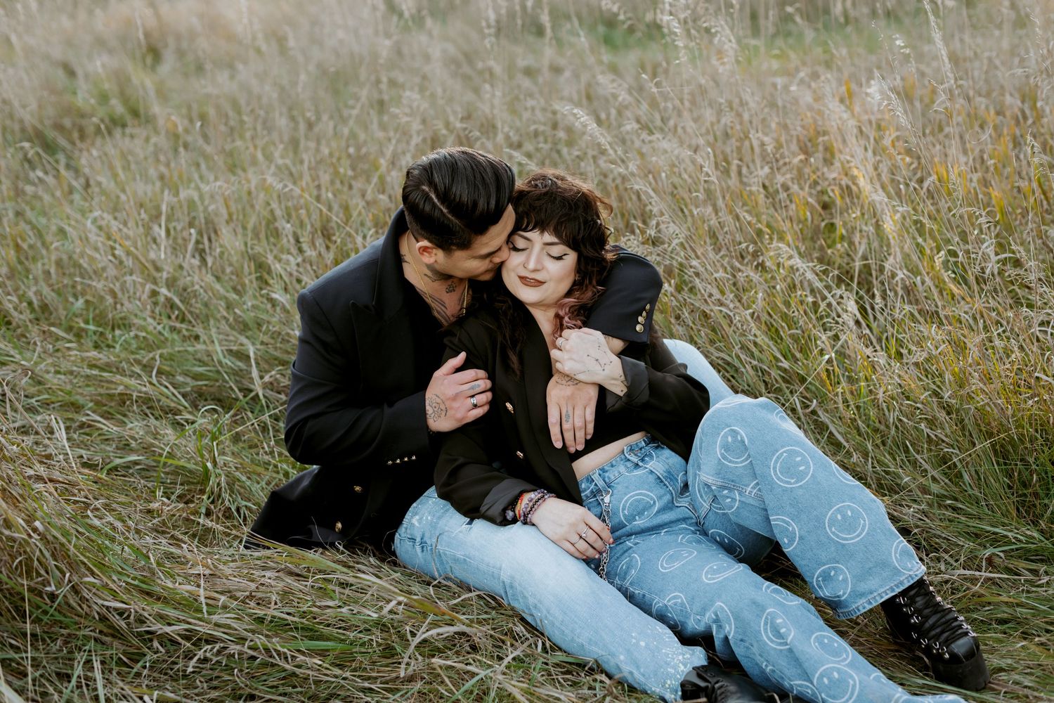 Couple cuddling in a field of tall grass during a golden hour photo session.