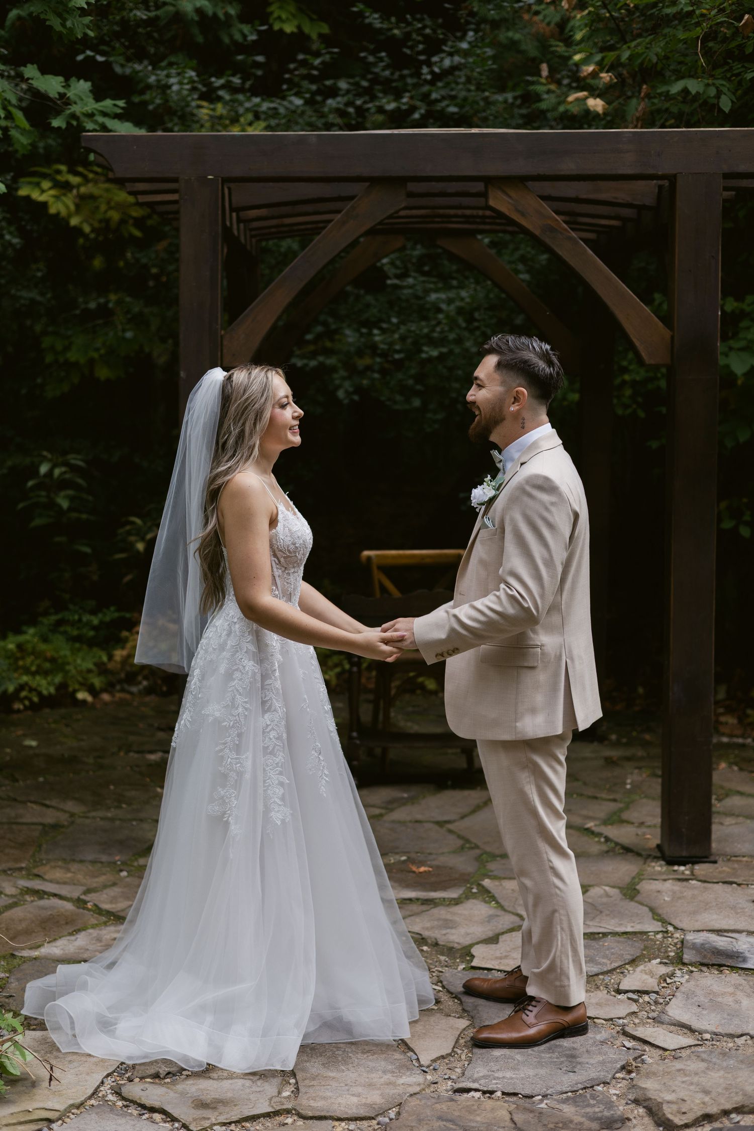 Bride and groom holding hands under wooden arch in lush garden during outdoor wedding ceremony.