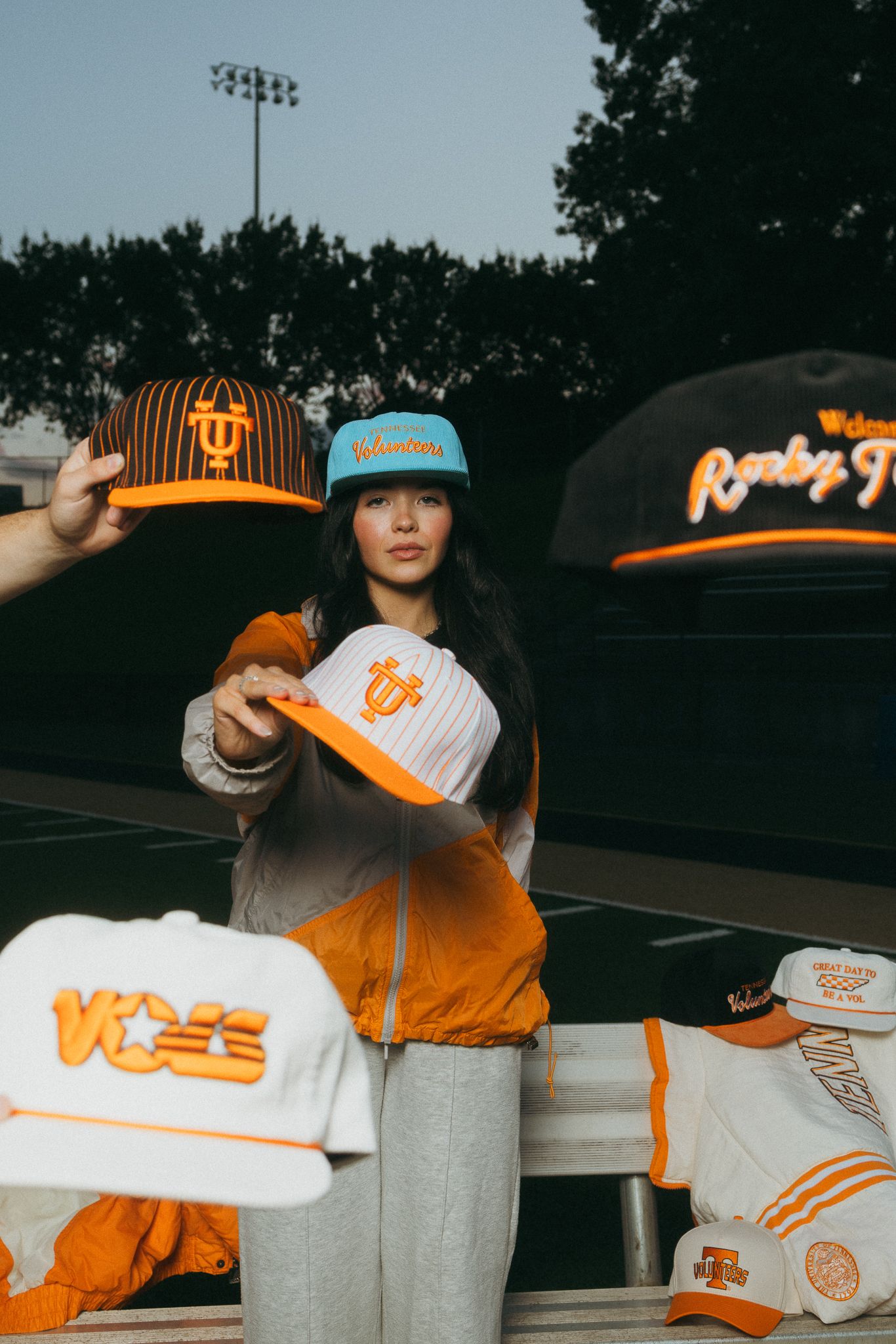 Woman holding Tennessee Volunteers fitted caps on a football field surrounded by orange and white hats.