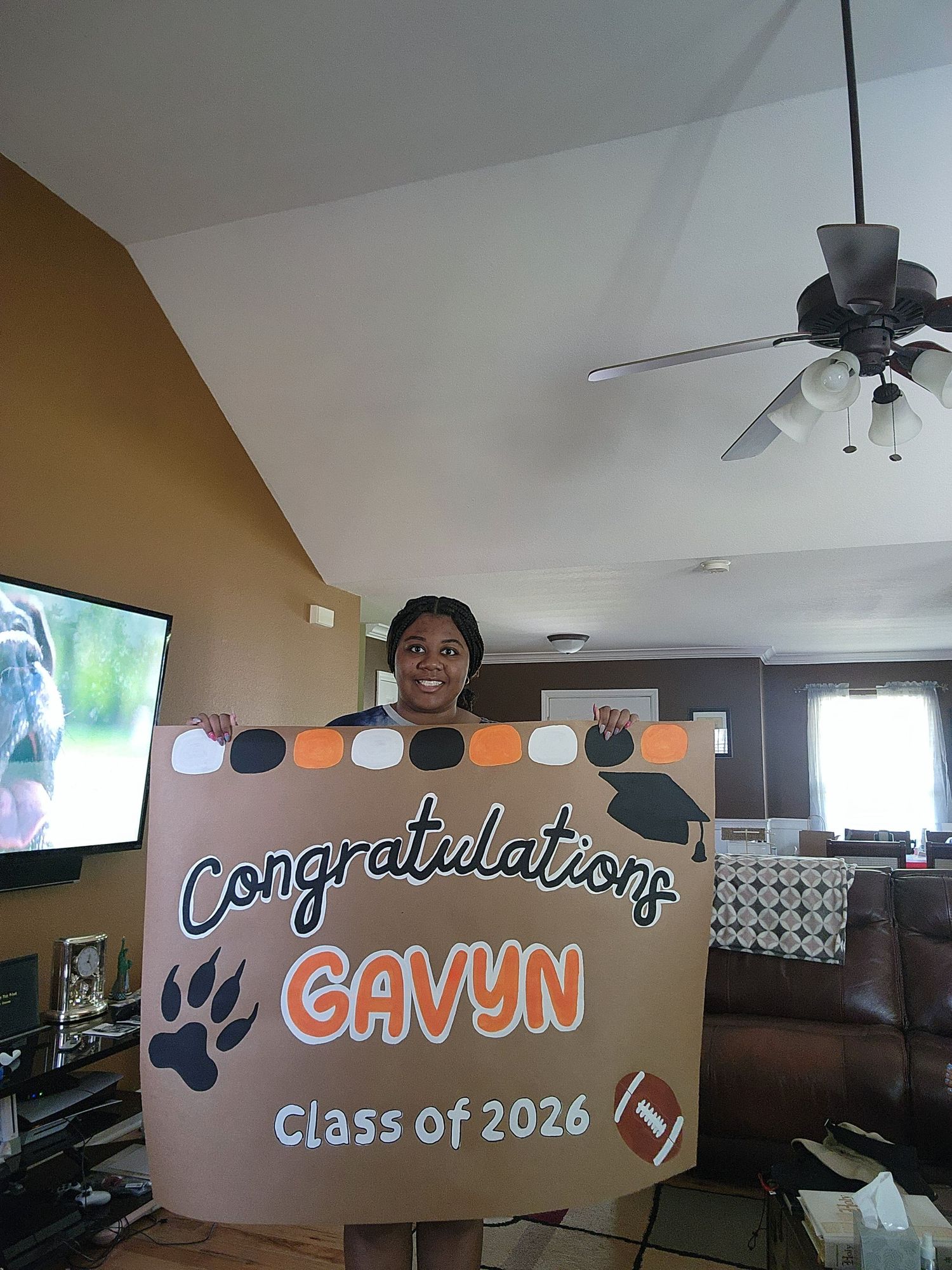 Person holding a Class of 2026 graduation banner congratulating Gavyn with a football and paw print design.