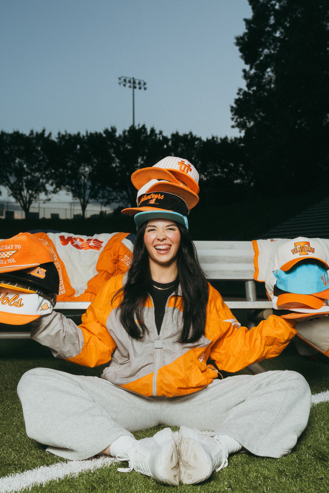 Woman laughing while holding multiple Tennessee Volunteers caps on a football field.