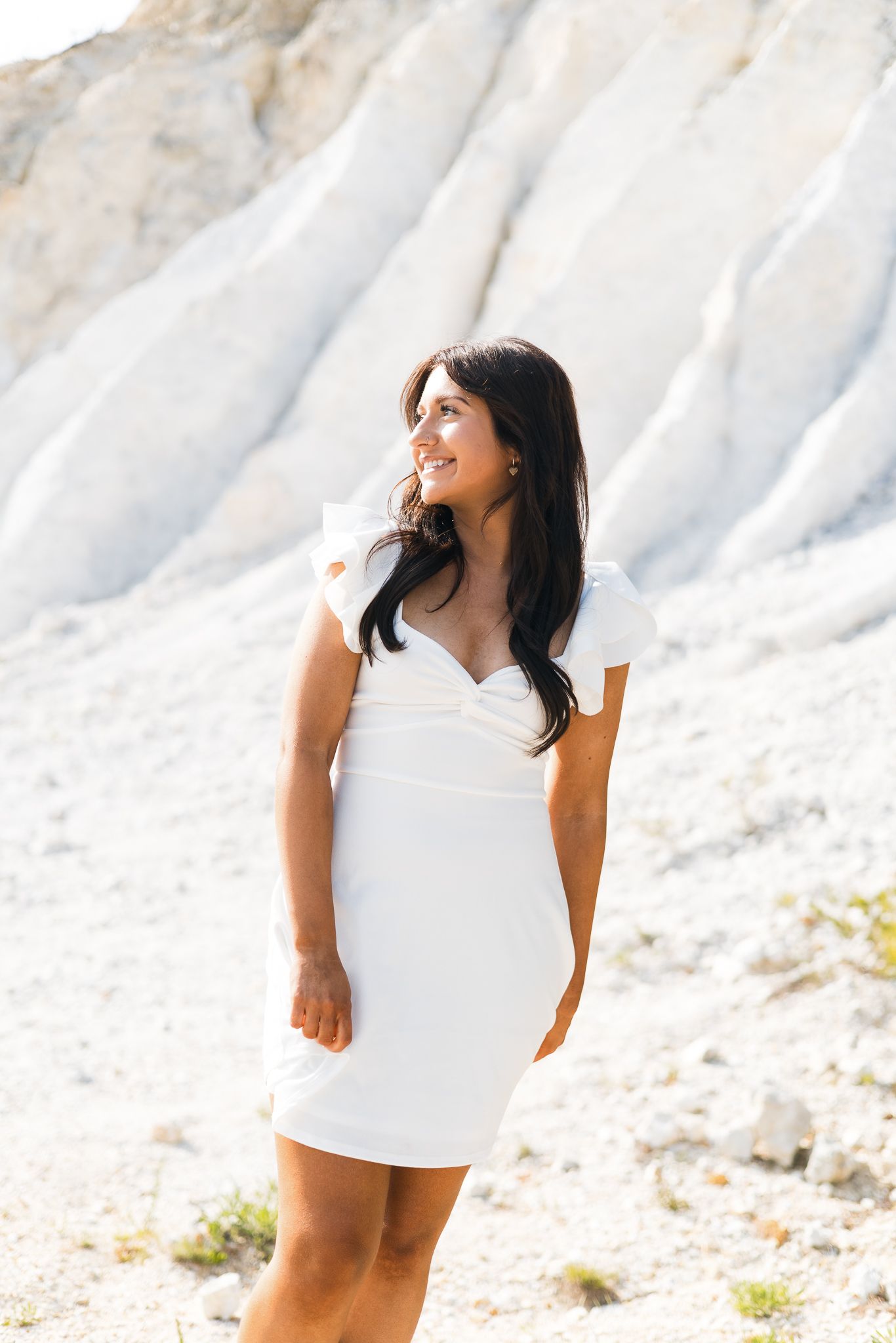 Young woman in white mini dress smiling outdoors against white rock formation.