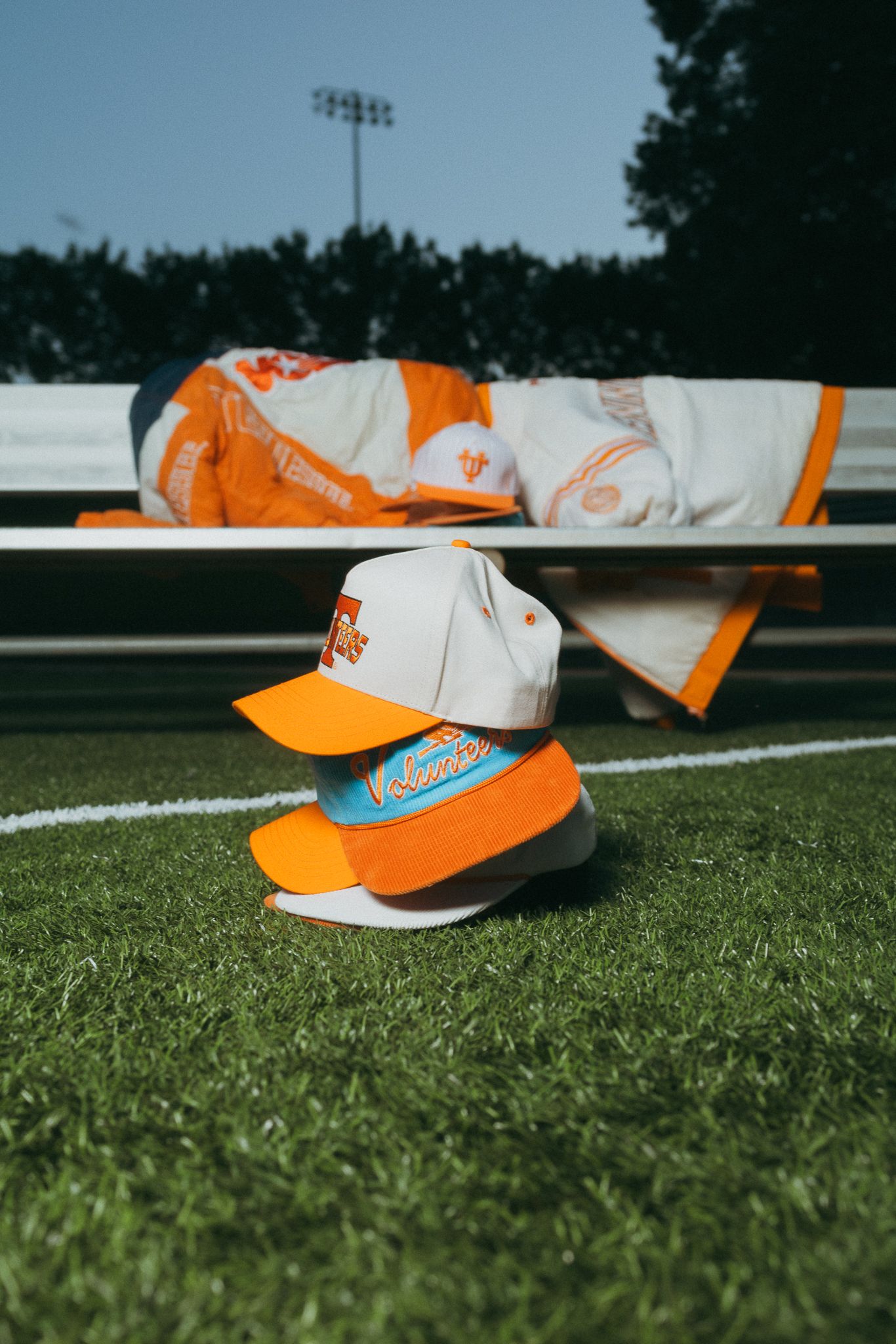 Two Tennessee Volunteers snapback caps stacked on green turf near a bench.