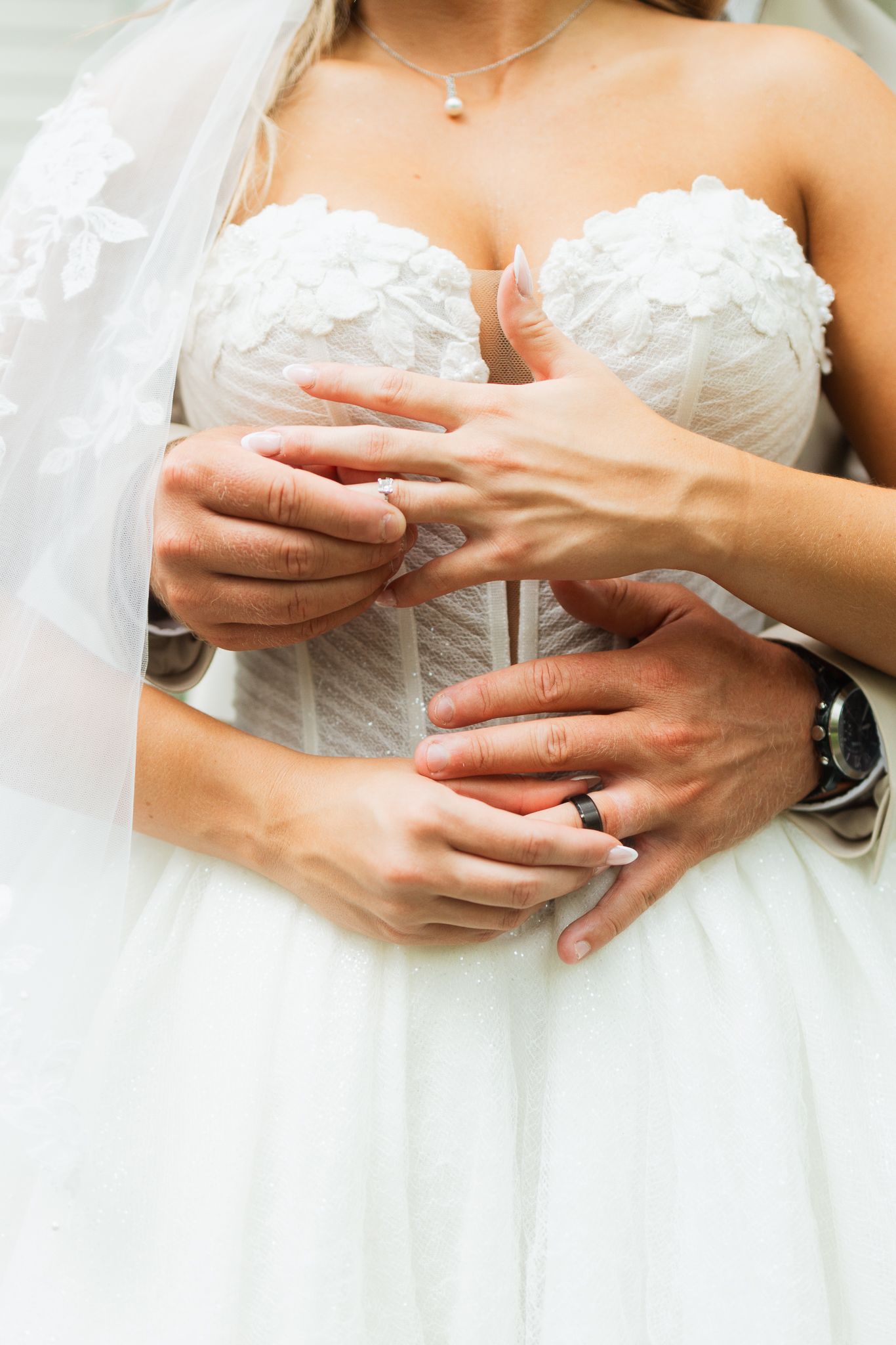 Bride and groom exchanging wedding rings, close-up of hands showing diamond ring and black band, white lace bridal gown.