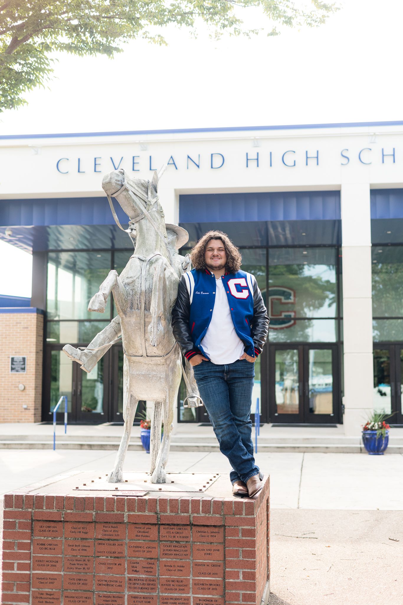 Student in a blue letterman jacket poses beside a horse statue outside Cleveland High School entrance.