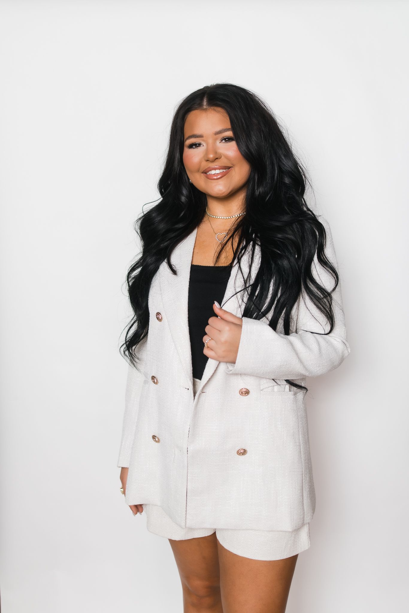 Smiling woman with long black hair wearing white double-breasted blazer and shorts set.