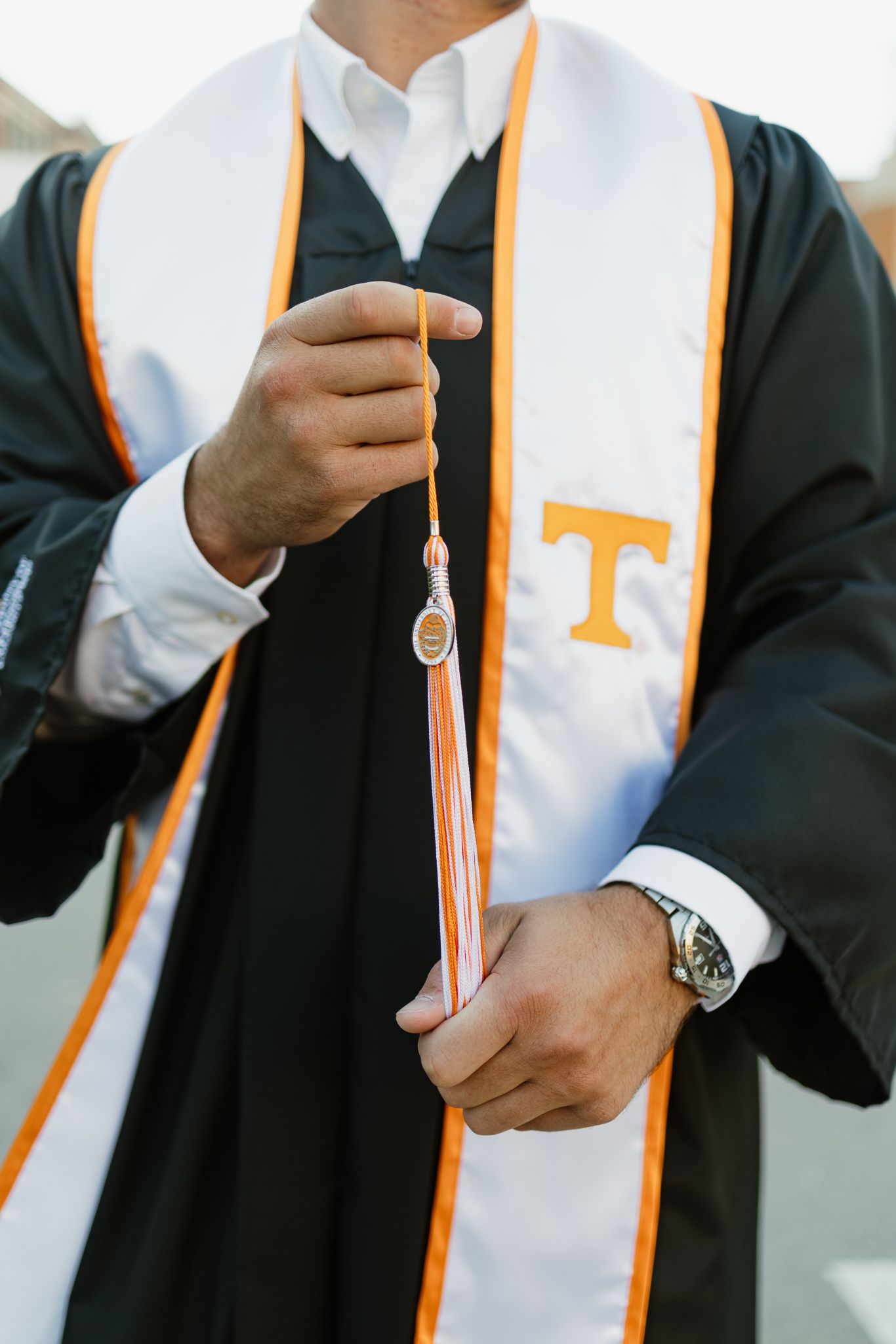 A University of Tennessee graduate holds an orange and white tassel while wearing a black graduation gown.
