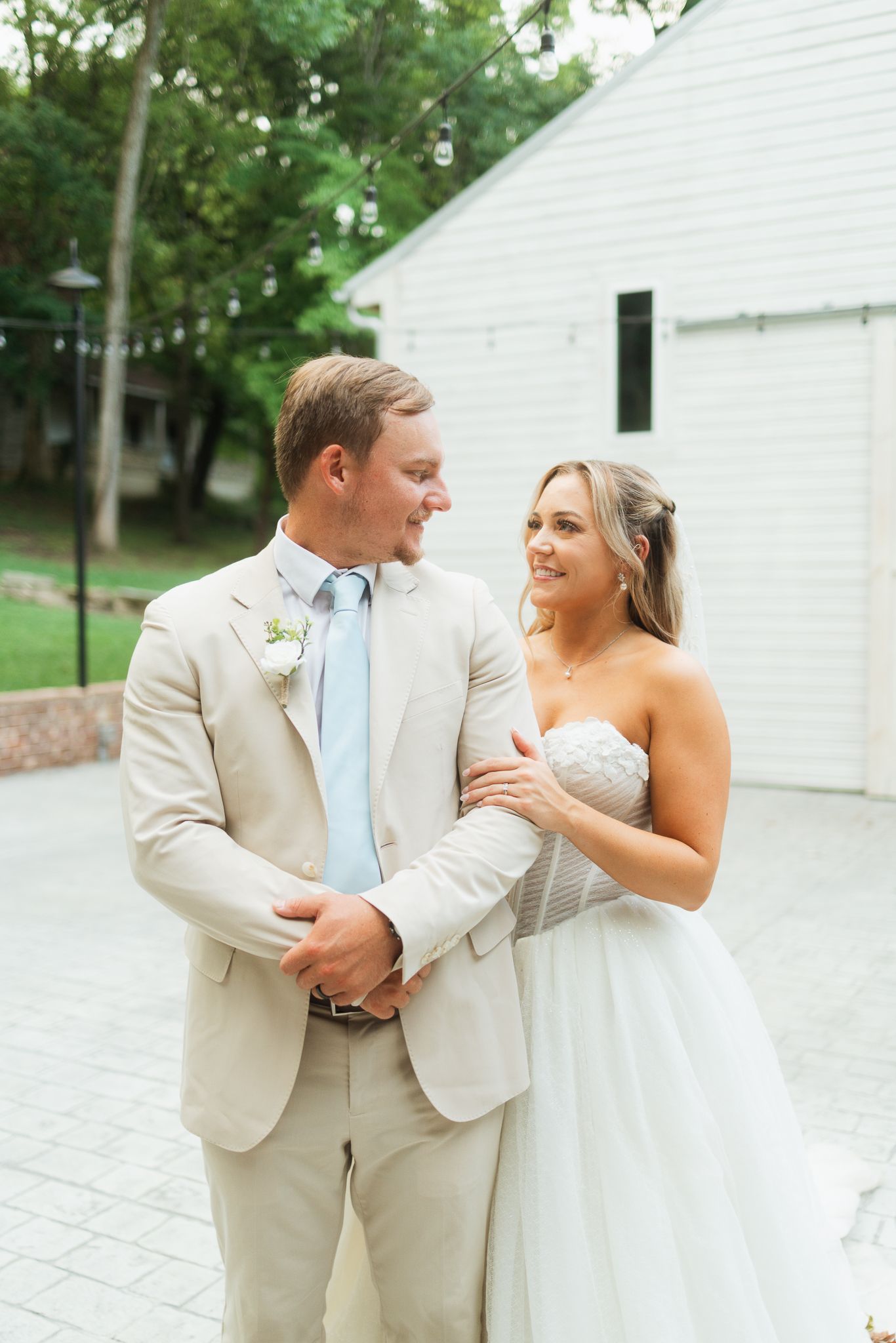 Bride in strapless gown and groom in tan suit with blue tie share a romantic moment outdoors at their wedding.