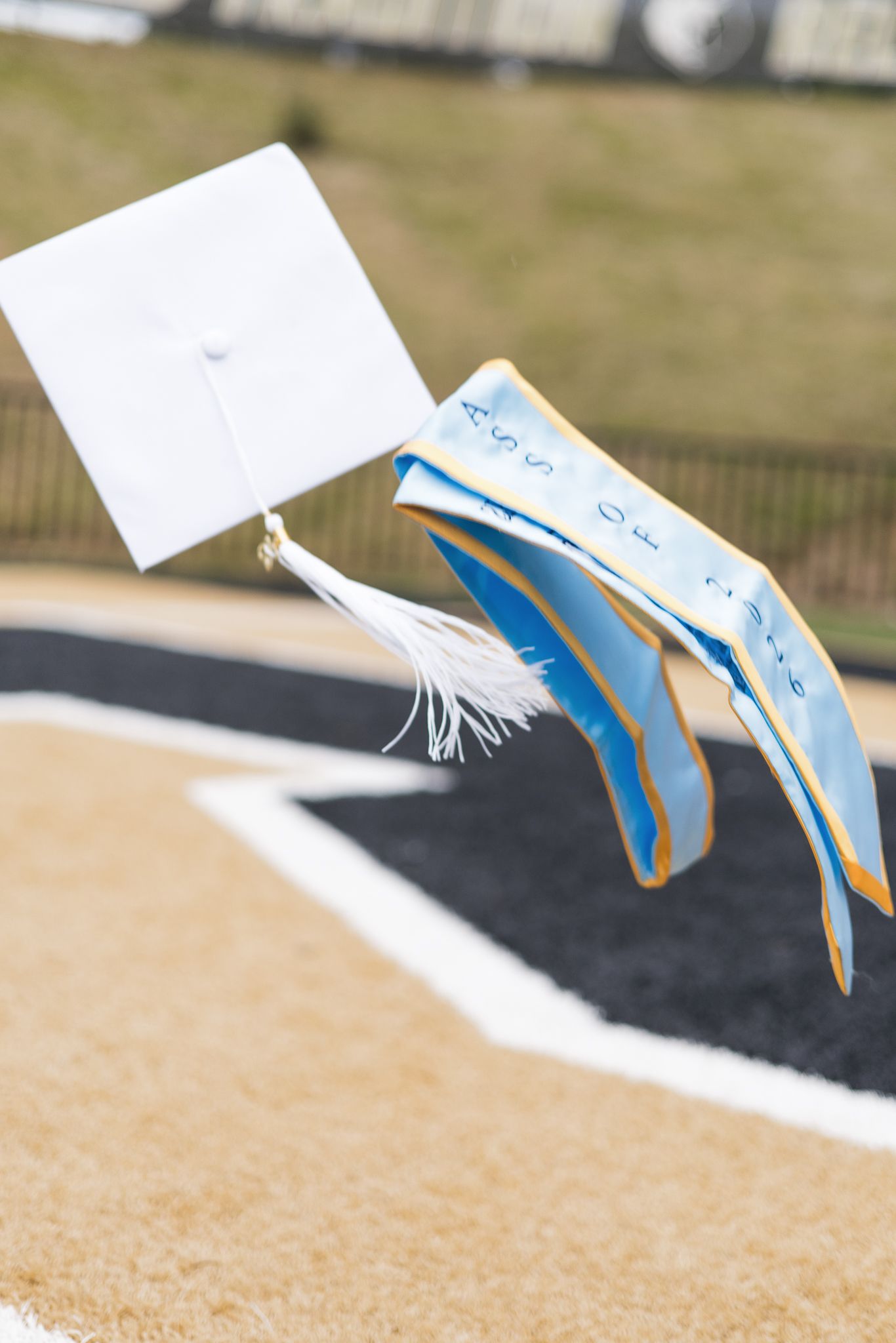 White graduation cap and blue stole with tassel flying through the air outdoors.