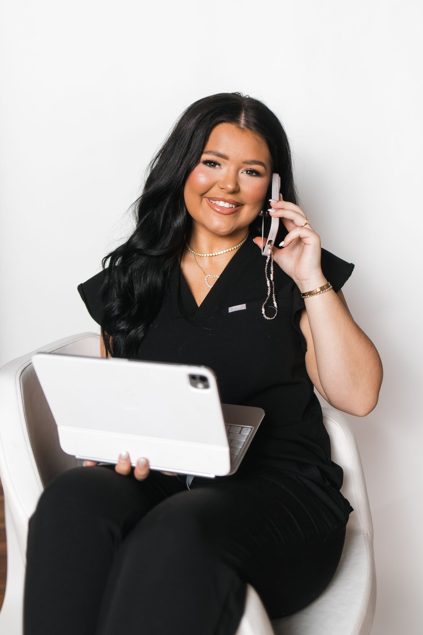 Professional woman in black scrubs smiles while talking on phone and holding a tablet.