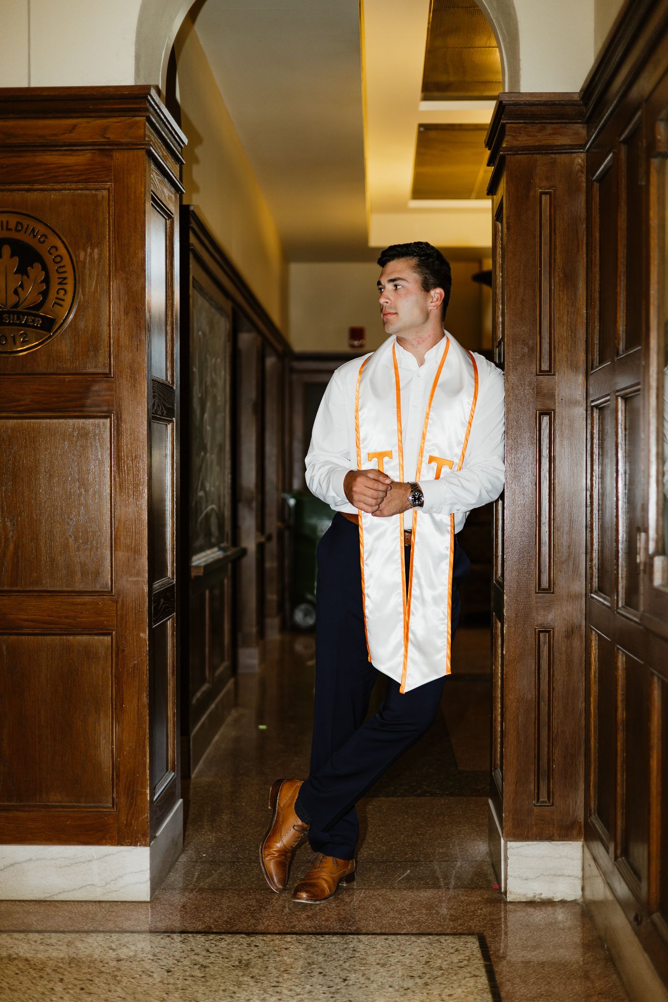 A University of Tennessee graduate stands in a wood-paneled hallway wearing his white and orange honor stole.