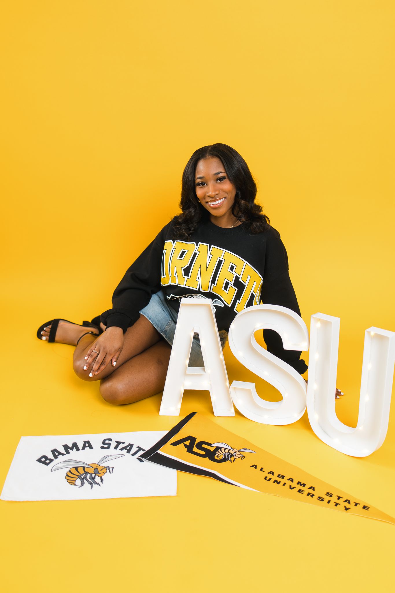 Smiling woman in ASU Hornets sweatshirt poses with Alabama State University letters and pennants on yellow background.