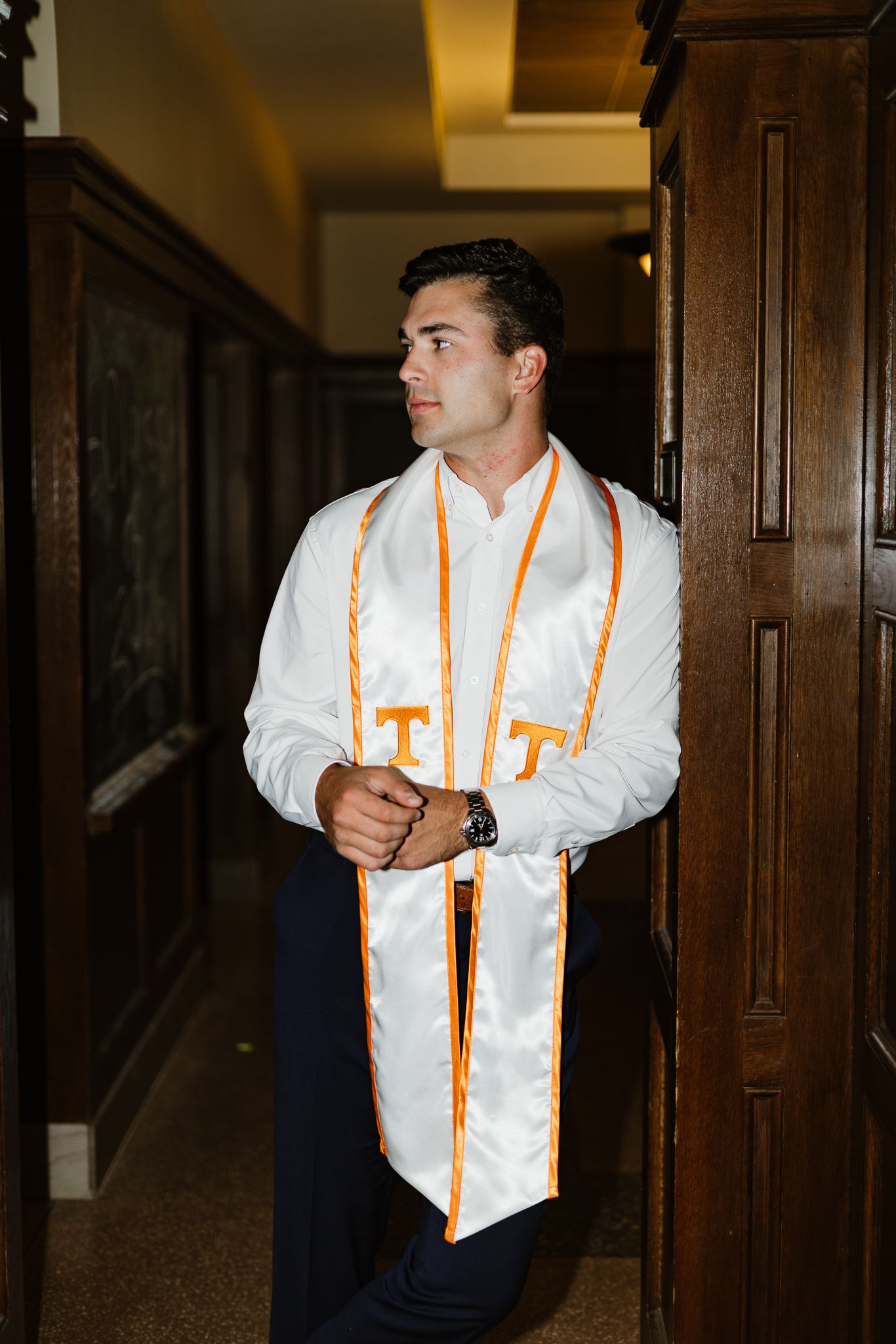 Young man in white University of Tennessee graduation stole and dress shirt leaning against wooden doorway.