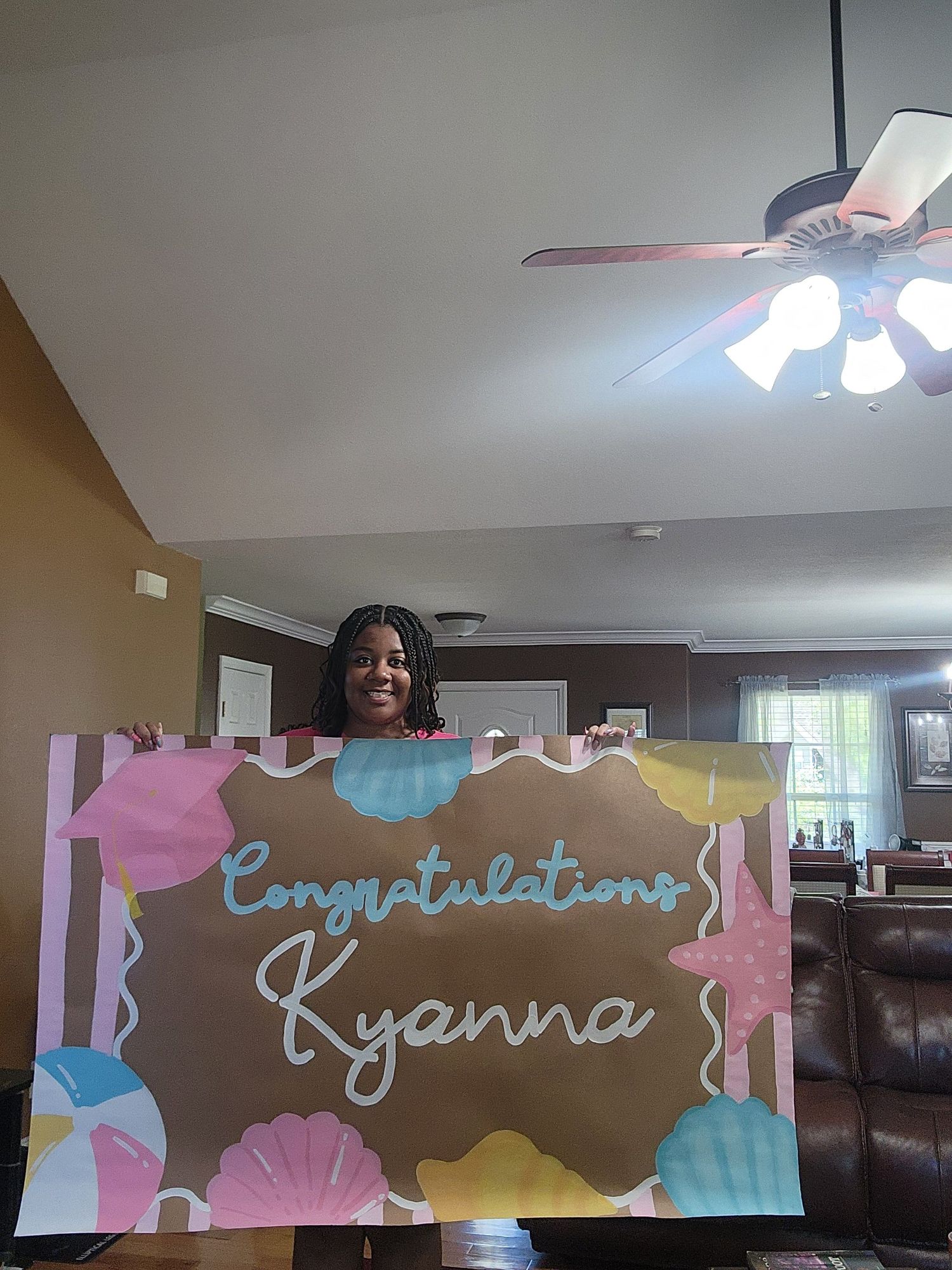 Woman holding a colorful Congratulations Kyanna banner at an indoor celebration party.
