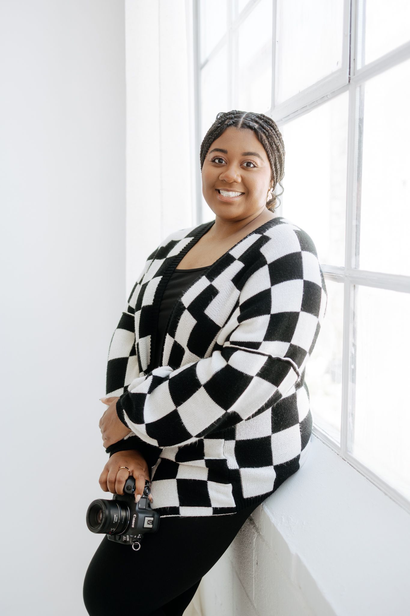 Plus-size Black woman photographer in black and white checkered cardigan posing with camera.