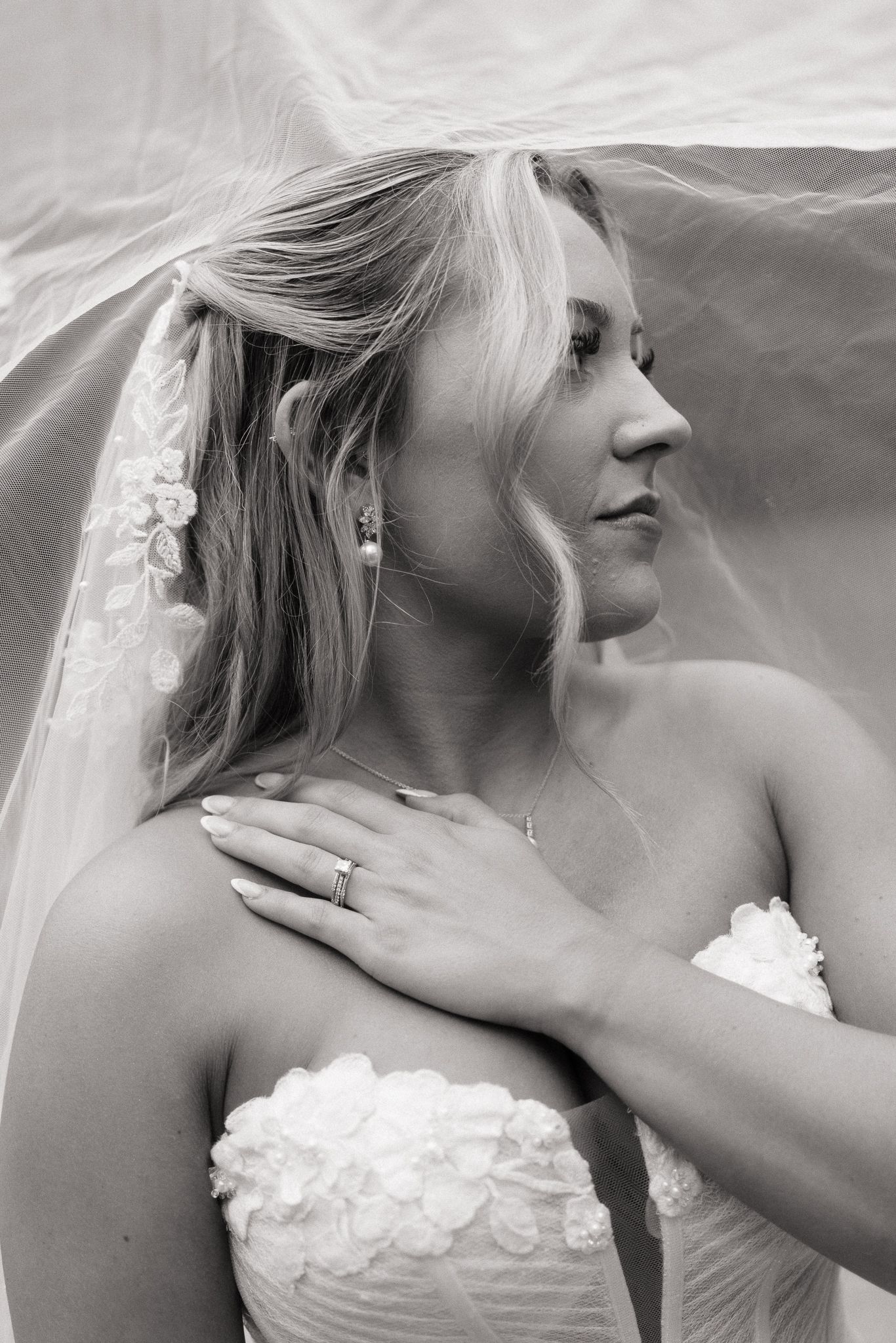 Black and white bridal portrait of blonde bride in strapless floral gown with veil, pearl earrings, and diamond ring.