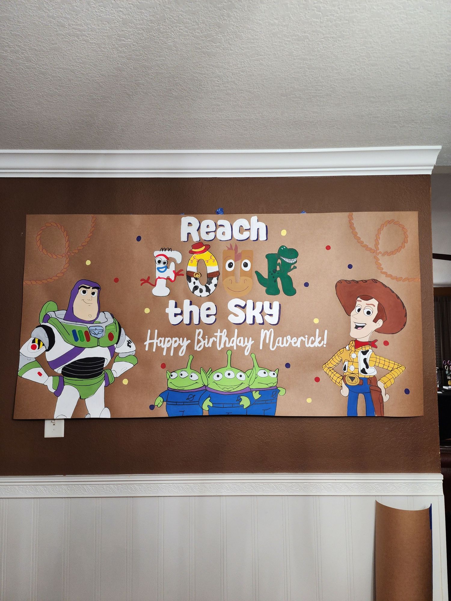 Toy Story themed birthday banner on wall reading Reach the Sky Happy Birthday Maverick with cartoon characters.